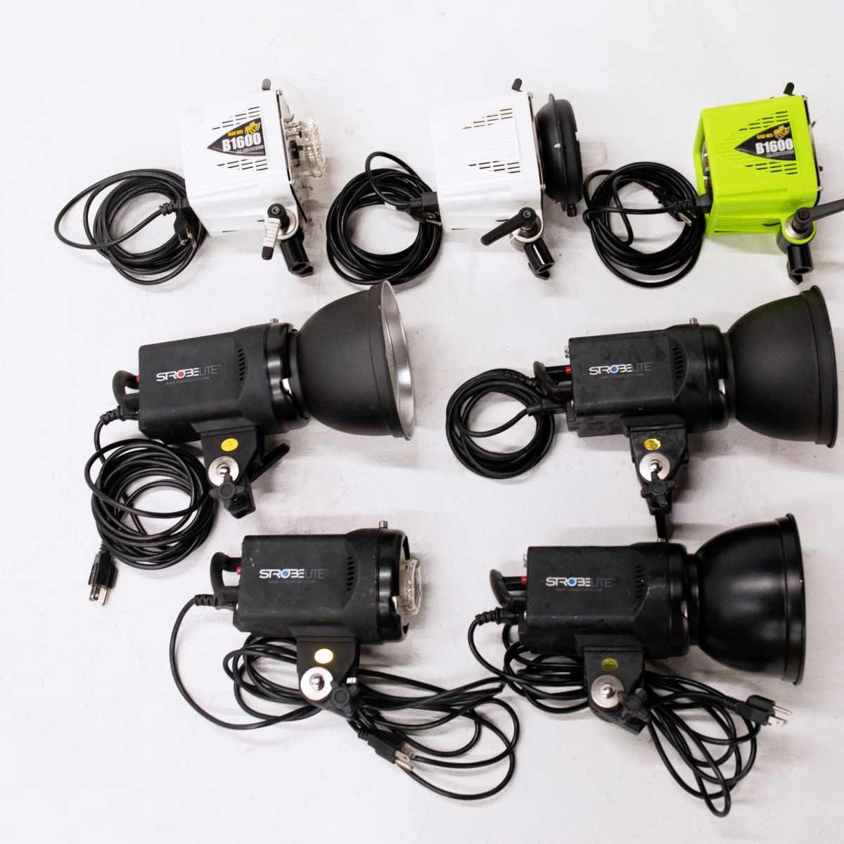 A layout of multiple lighting fixtures, including three black lights with reflectors and several small white and green control units, all connected by cables on a white surface.