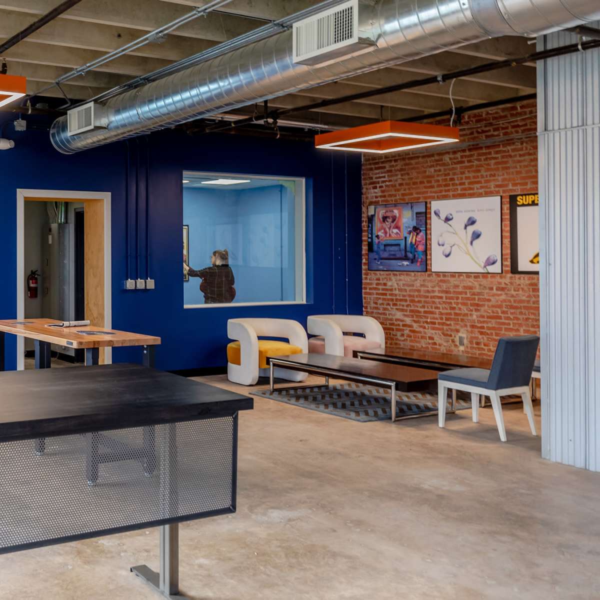 A modern office space with a black desk, several seating areas, and blue and brick walls.