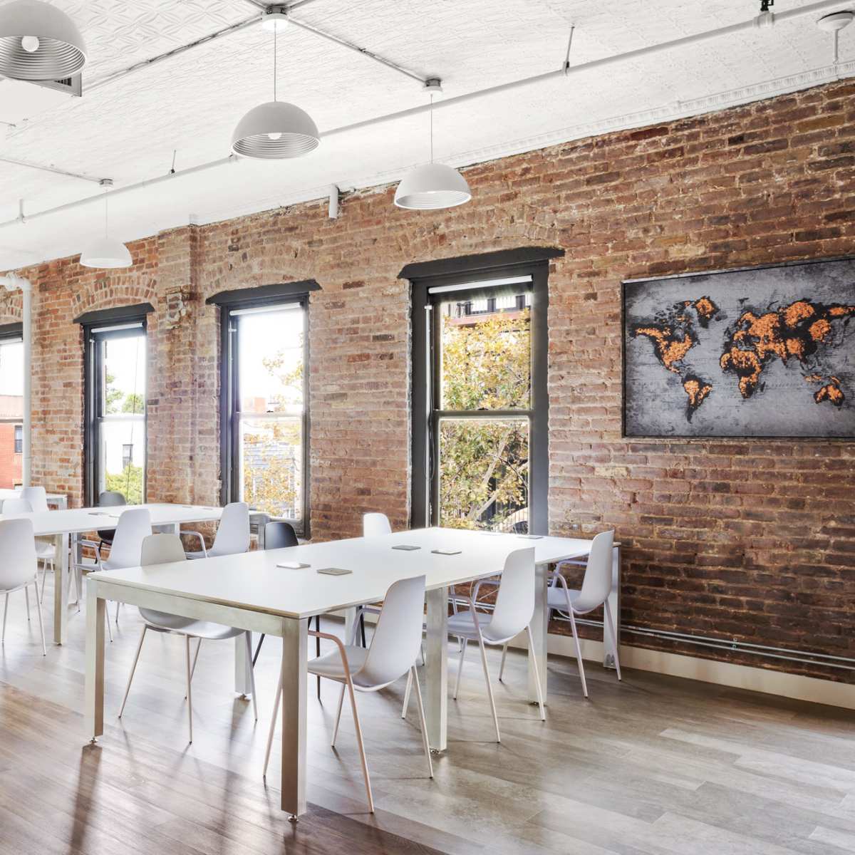 A bright, modern dining area features white tables and chairs against a backdrop of exposed brick walls and large windows.