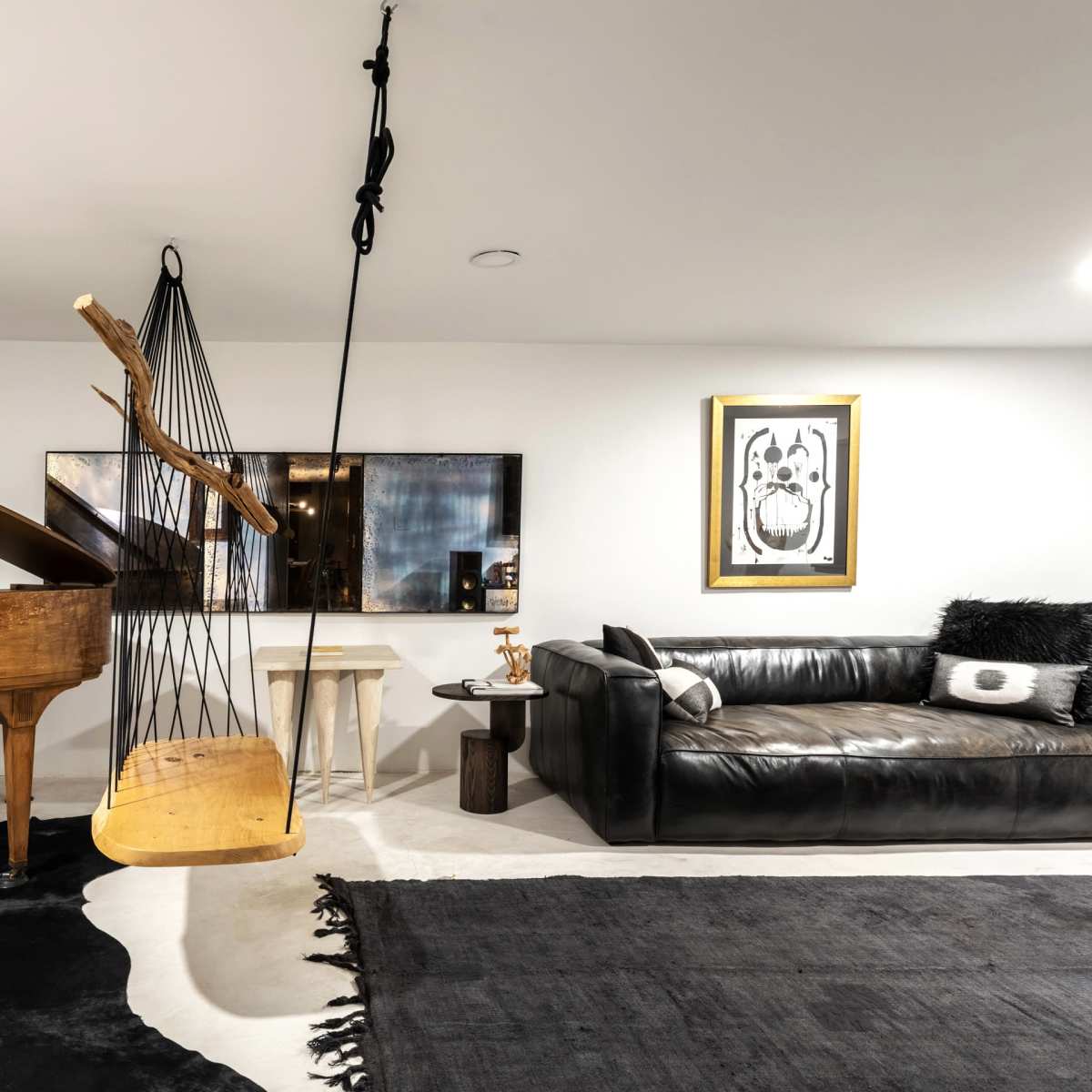 A modern living space featuring a grand piano, a black leather sofa, a wall-mounted artwork, and a unique hanging sculpture.