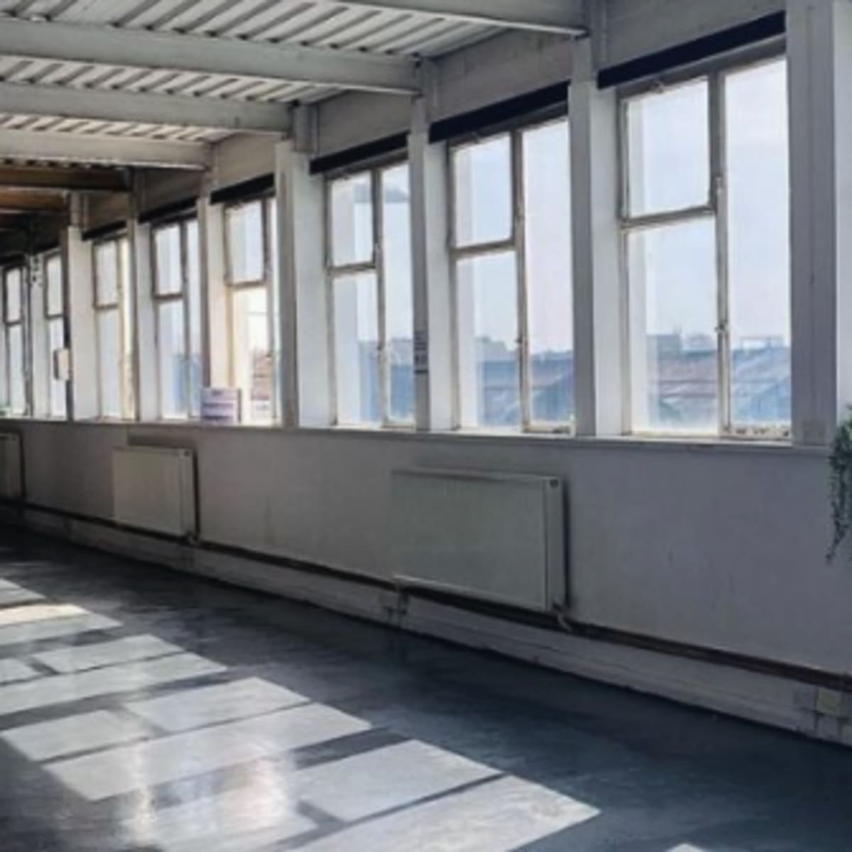 A corridor with large windows along one side, allowing natural light to illuminate the space and casting shadows on the floor.