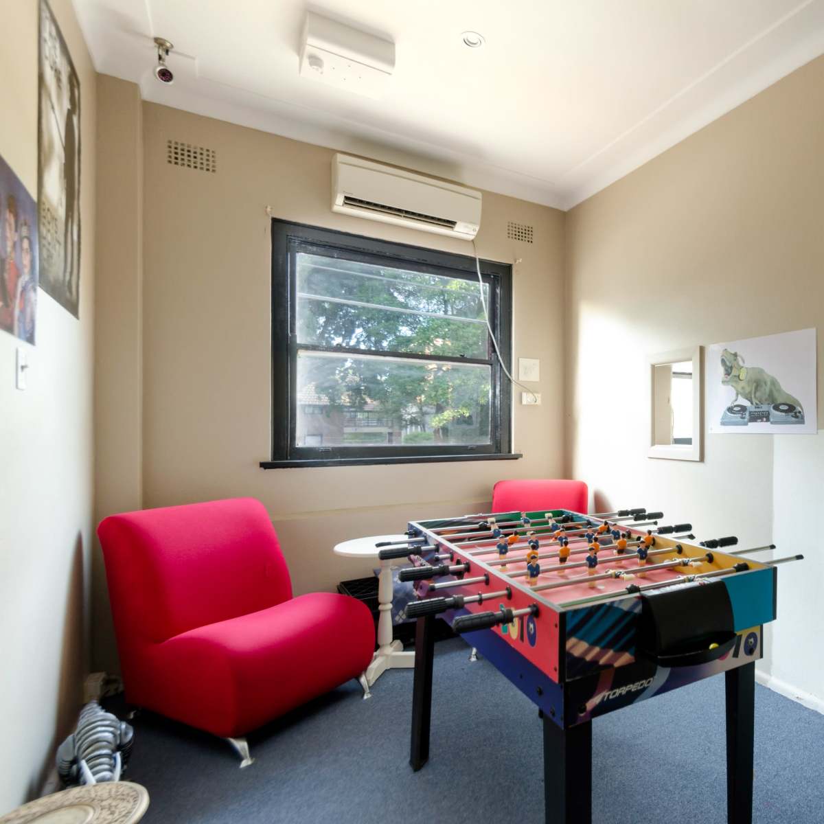 A small, tidy room with a foosball table, a red couch, and an open doorway leading to another room featuring filing cabinets.