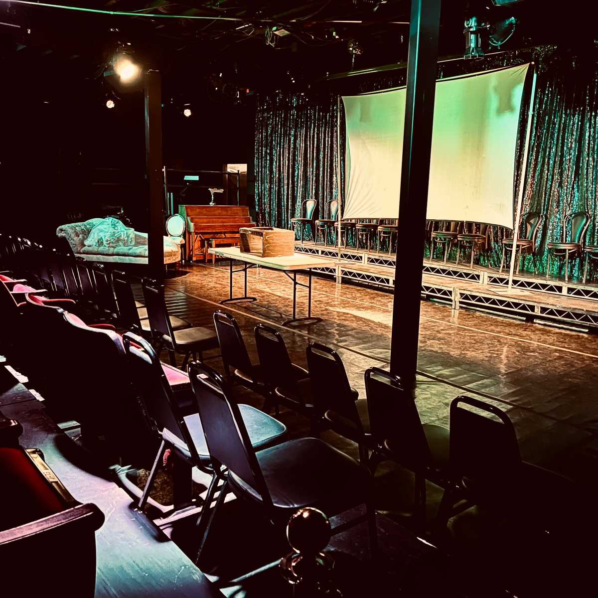 A performance space with rows of chairs facing a stage that has a large screen and a glittering curtain backdrop.