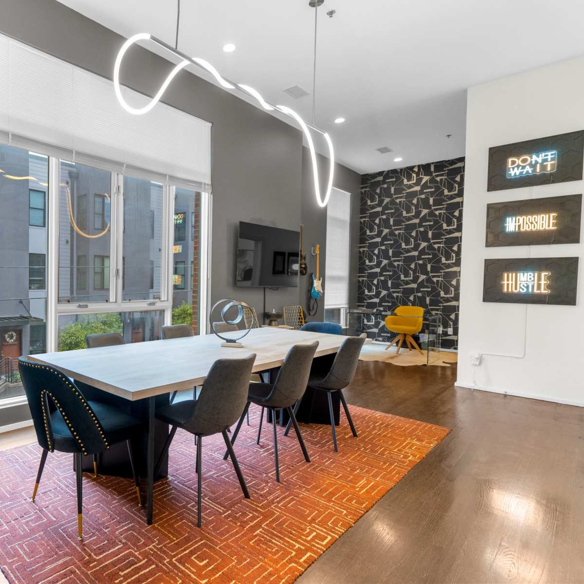 A modern dining area features a long table surrounded by upholstered chairs, set against a backdrop of large windows and creatively designed wall decor.
