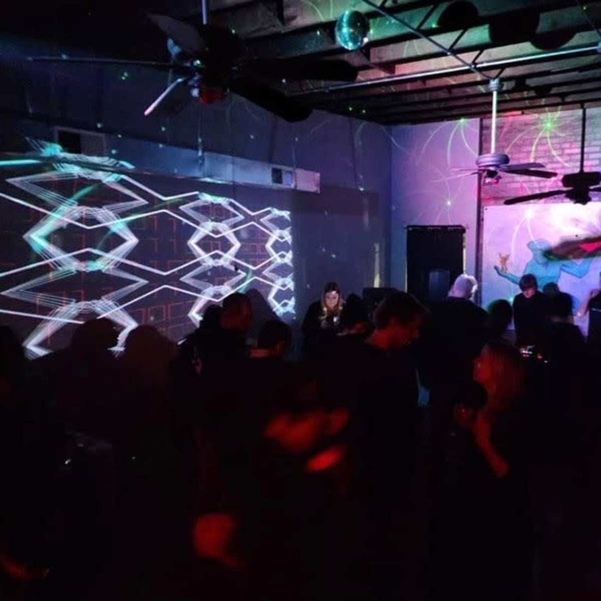 A dimly lit indoor space with people dancing and colorful light projections on the walls.