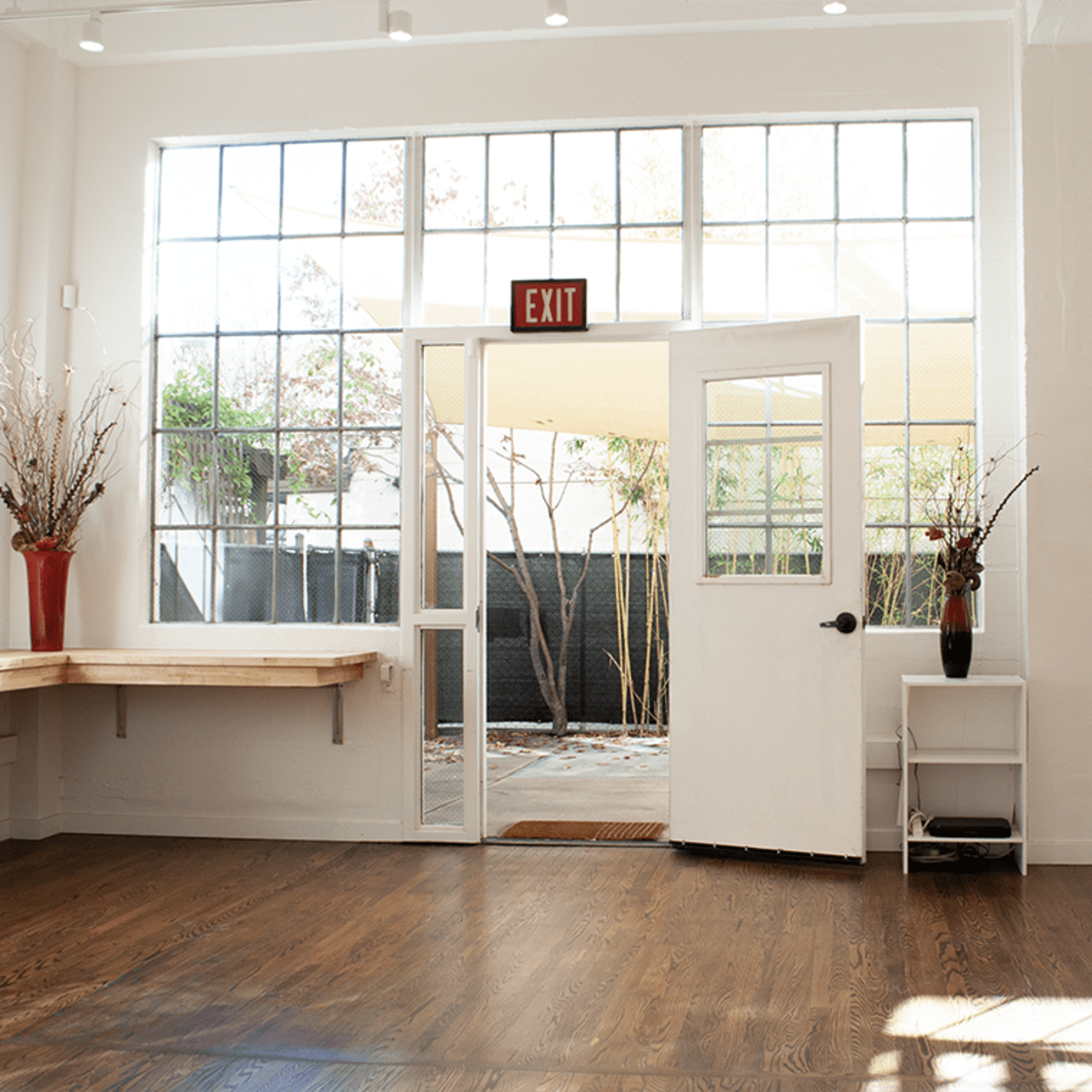 A bright, airy room with large windows, a white door leading outside, and wooden flooring.