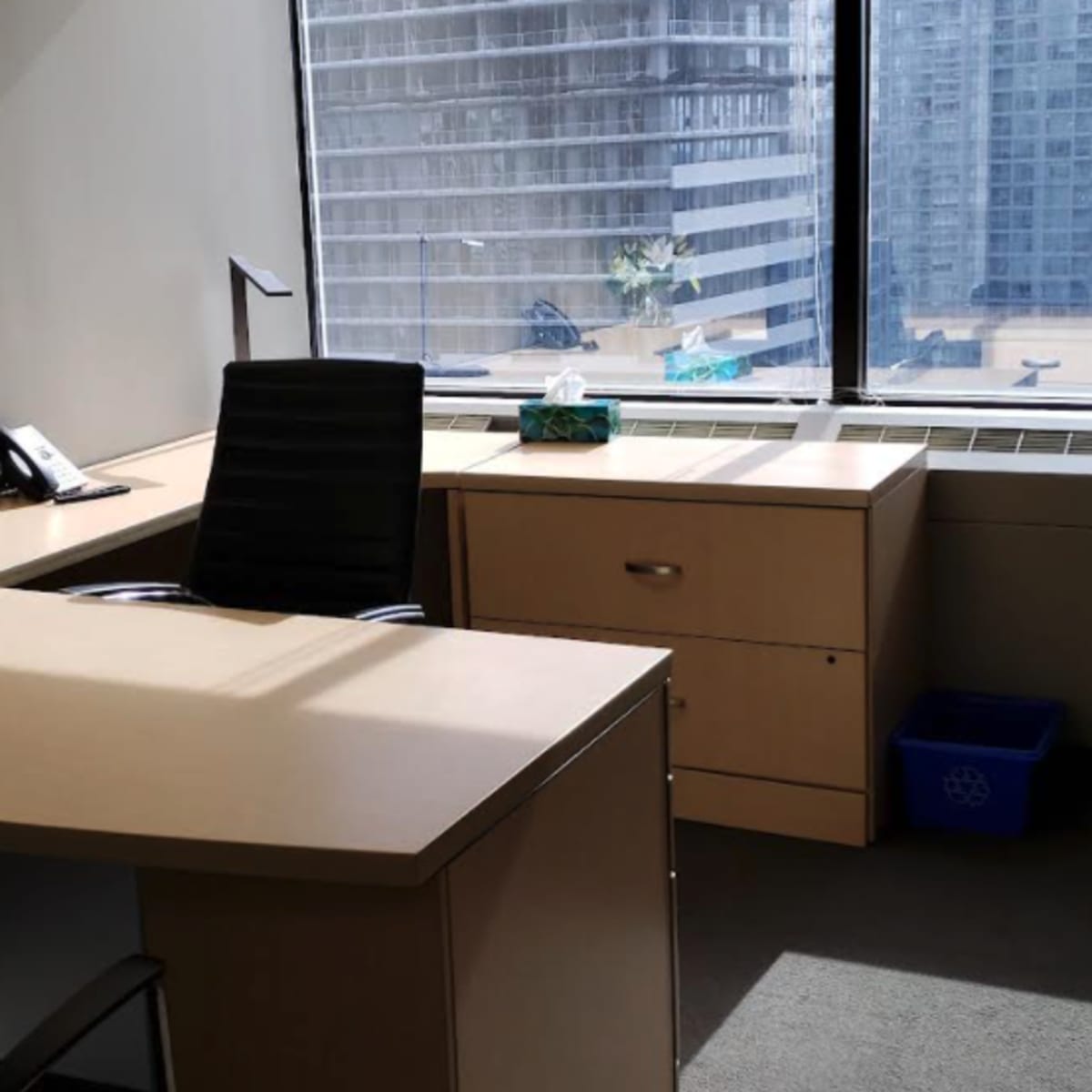 A modern office space with a desk, chair, and window displaying a view of tall buildings outside.