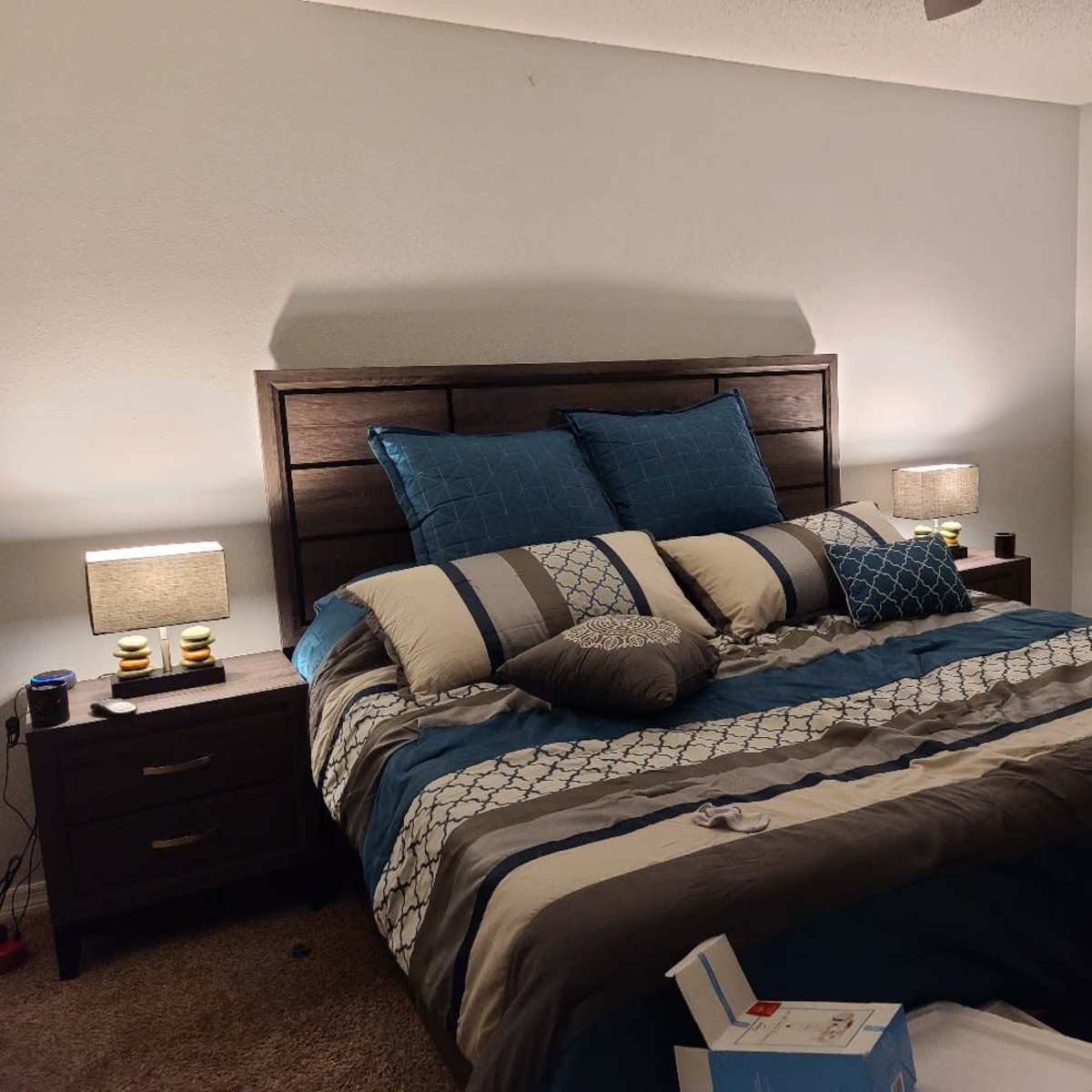 A neatly made bed with blue and gray bedding is centered in a softly lit bedroom, flanked by two bedside tables with lamps.