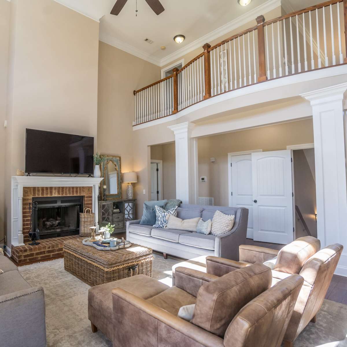A spacious living room with a high ceiling, a fireplace, large windows, and comfortable seating arrangements.