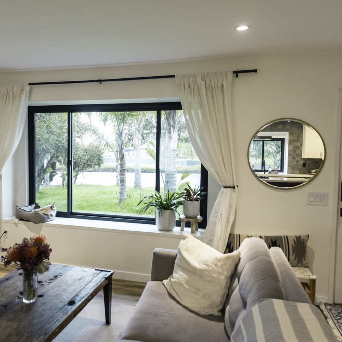 A living room features a large window overlooking a green yard, with a coffee table, sofa, and television present in the space.