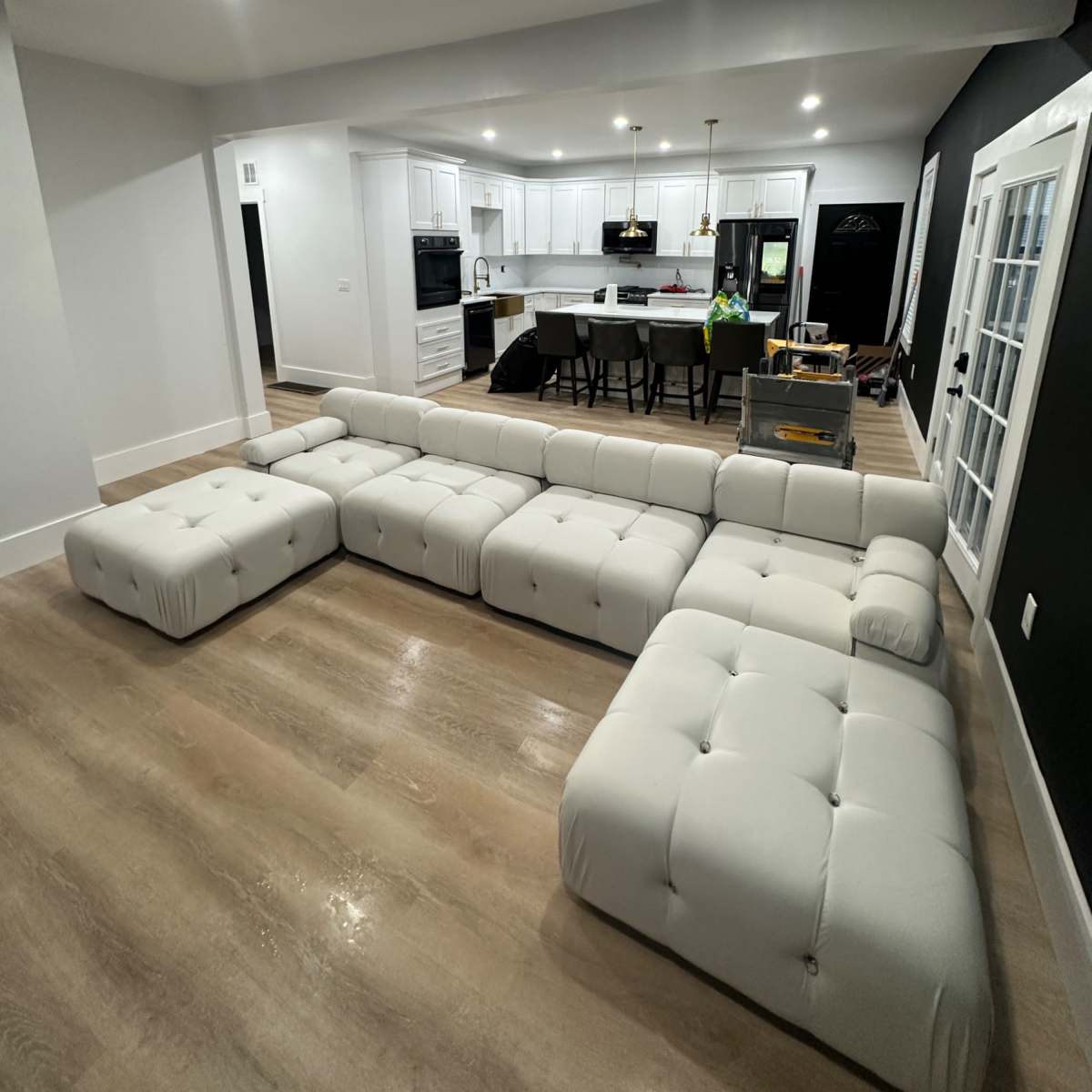 A white tufted sectional sofa is positioned in a modern, open-concept kitchen and living area.