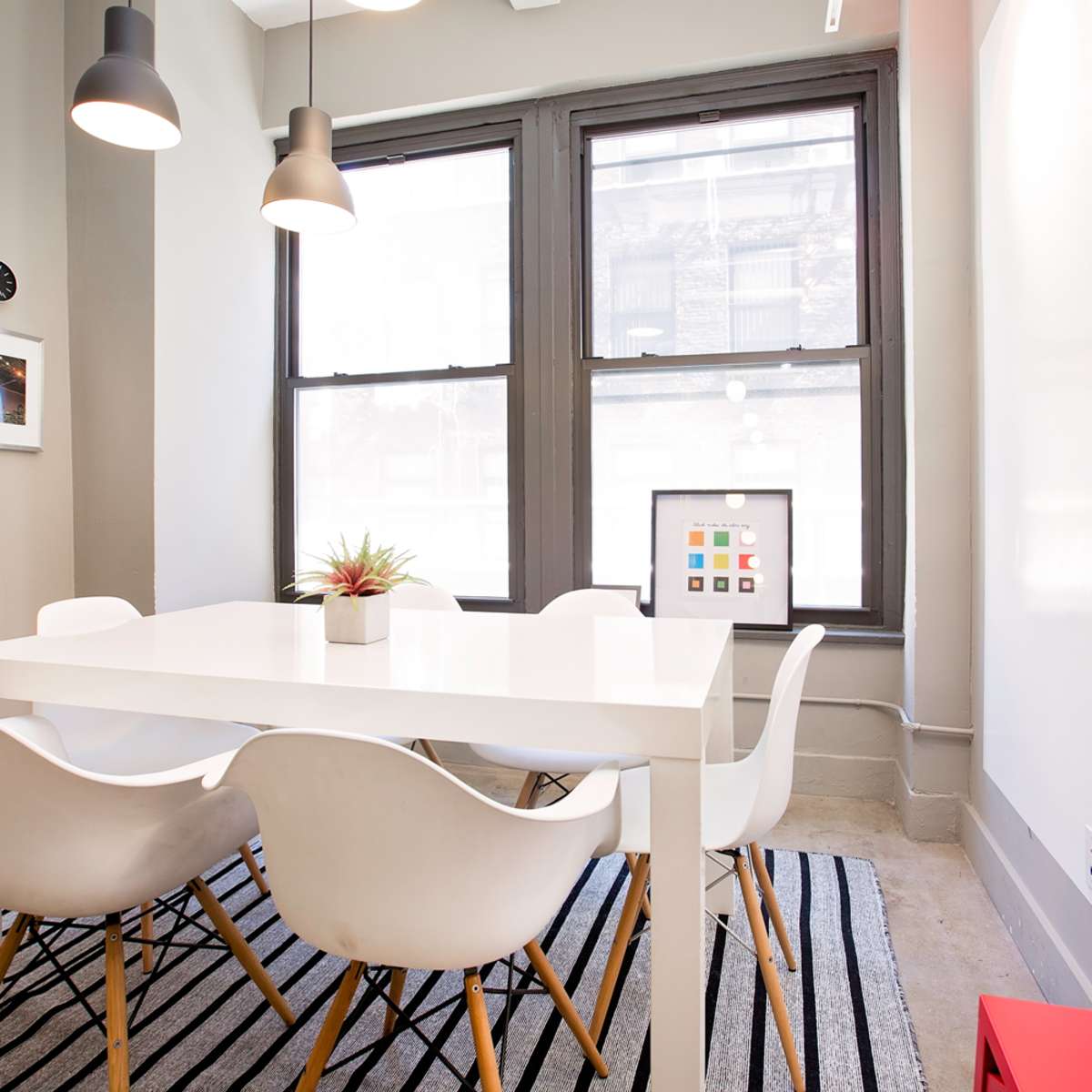 A modern dining area features a white table surrounded by six white chairs, with large windows and a patterned rug on the floor.