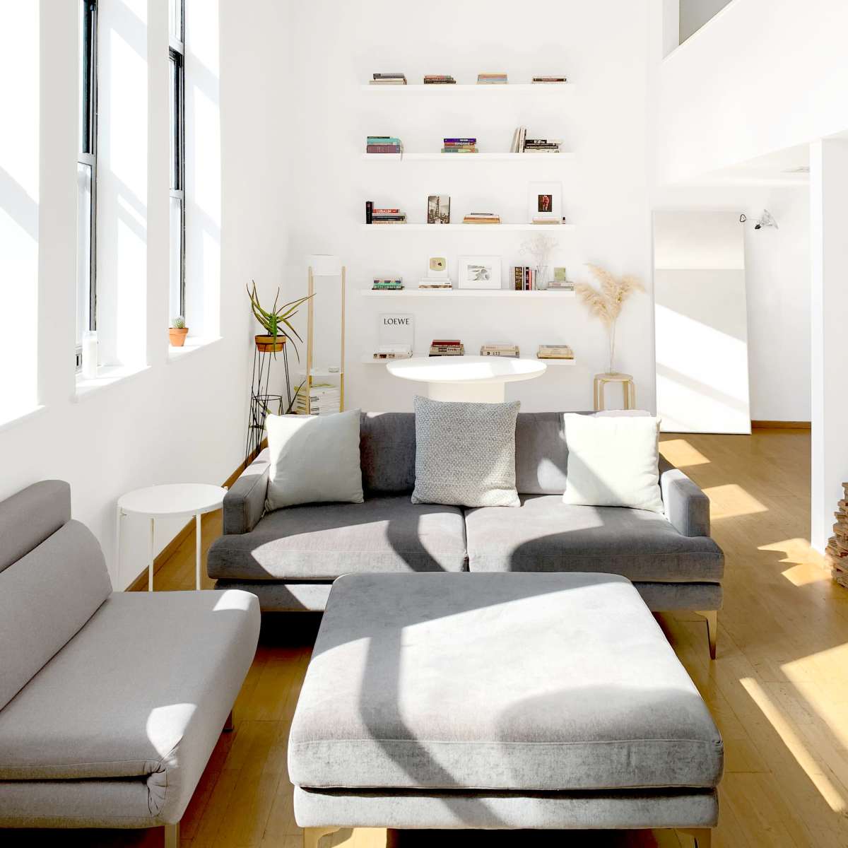A bright, minimalist living room with a gray sofa, a coffee table, and shelves displaying books and decorative items against white walls.