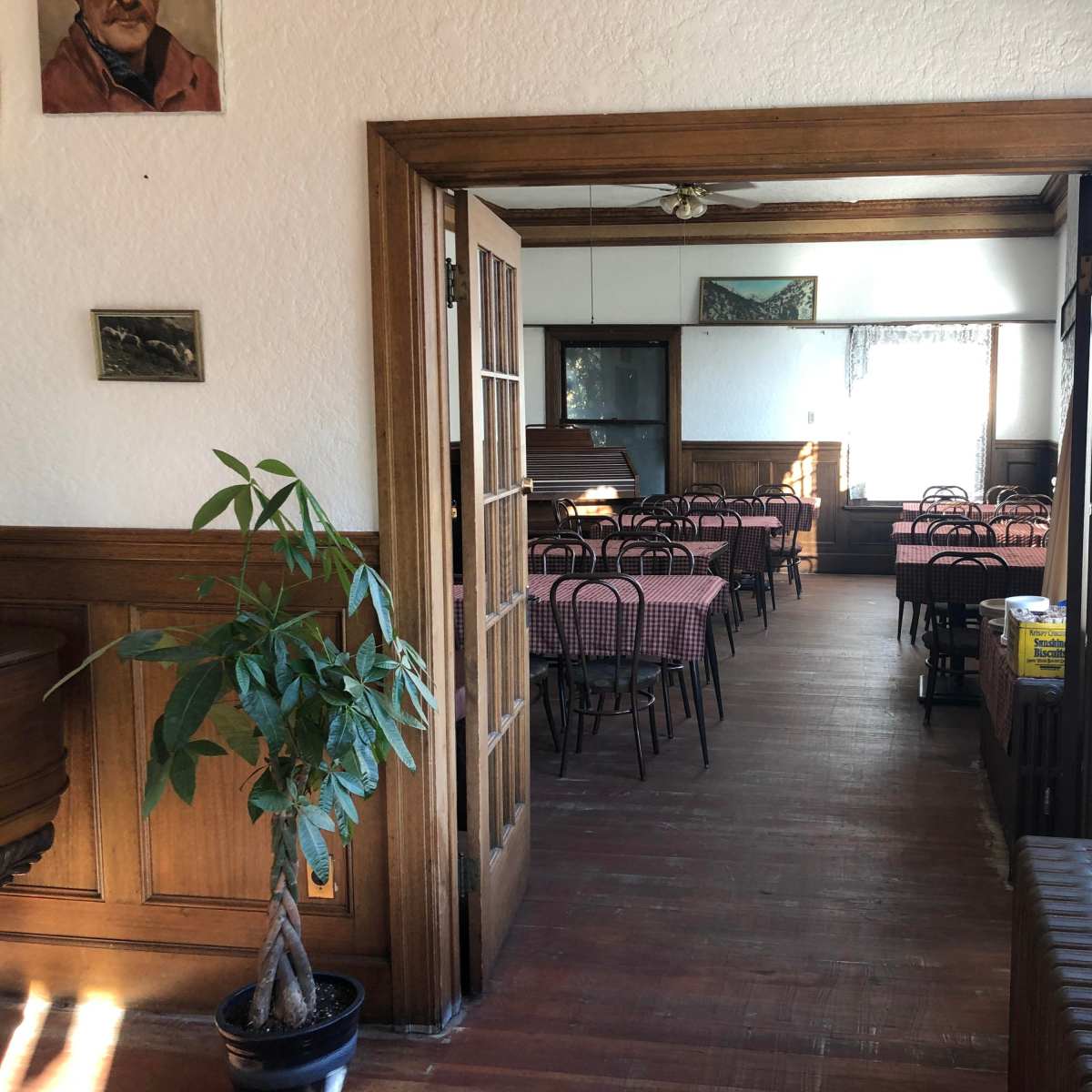 An empty dining area with checkered tablecloths and wooden furniture, featuring large windows and wooden paneling.