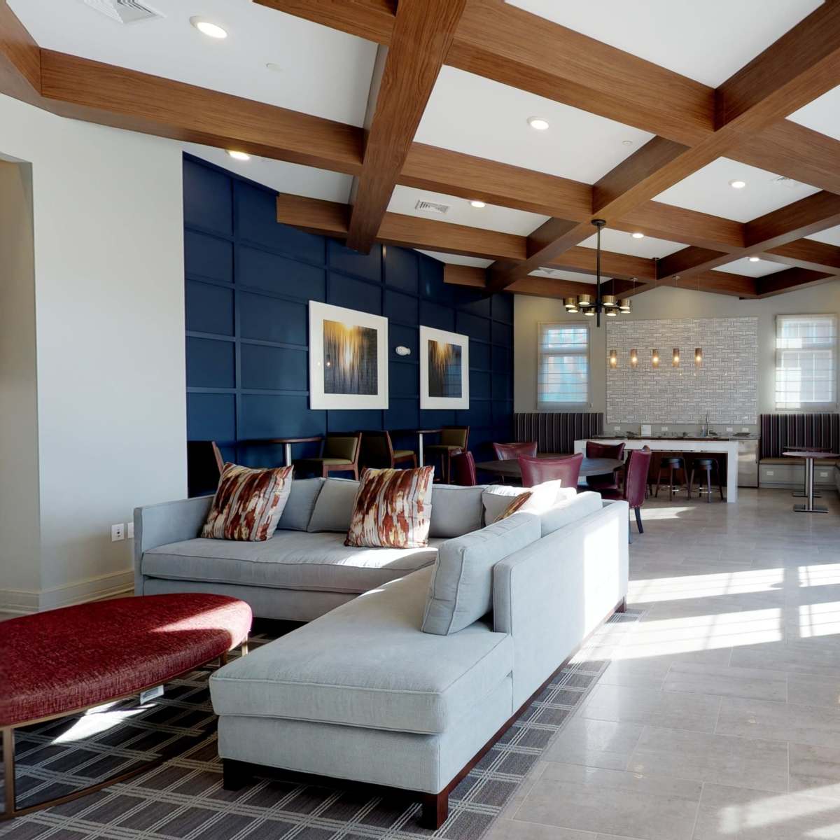 A modern lounge area features a sectional sofa, wooden beams on the ceiling, and a dining area with a large table and chairs.