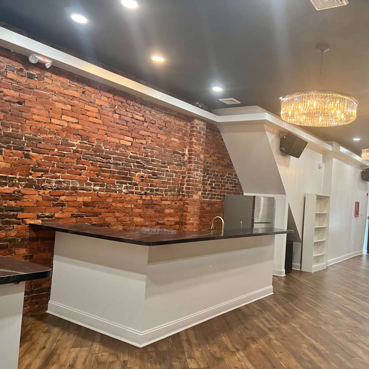 The interior features a brick wall, a bar area, and large windows draped with white curtains.