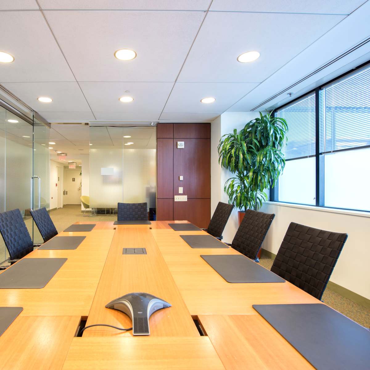 A large conference room features a wooden table surrounded by black leather chairs and is illuminated by overhead lights.