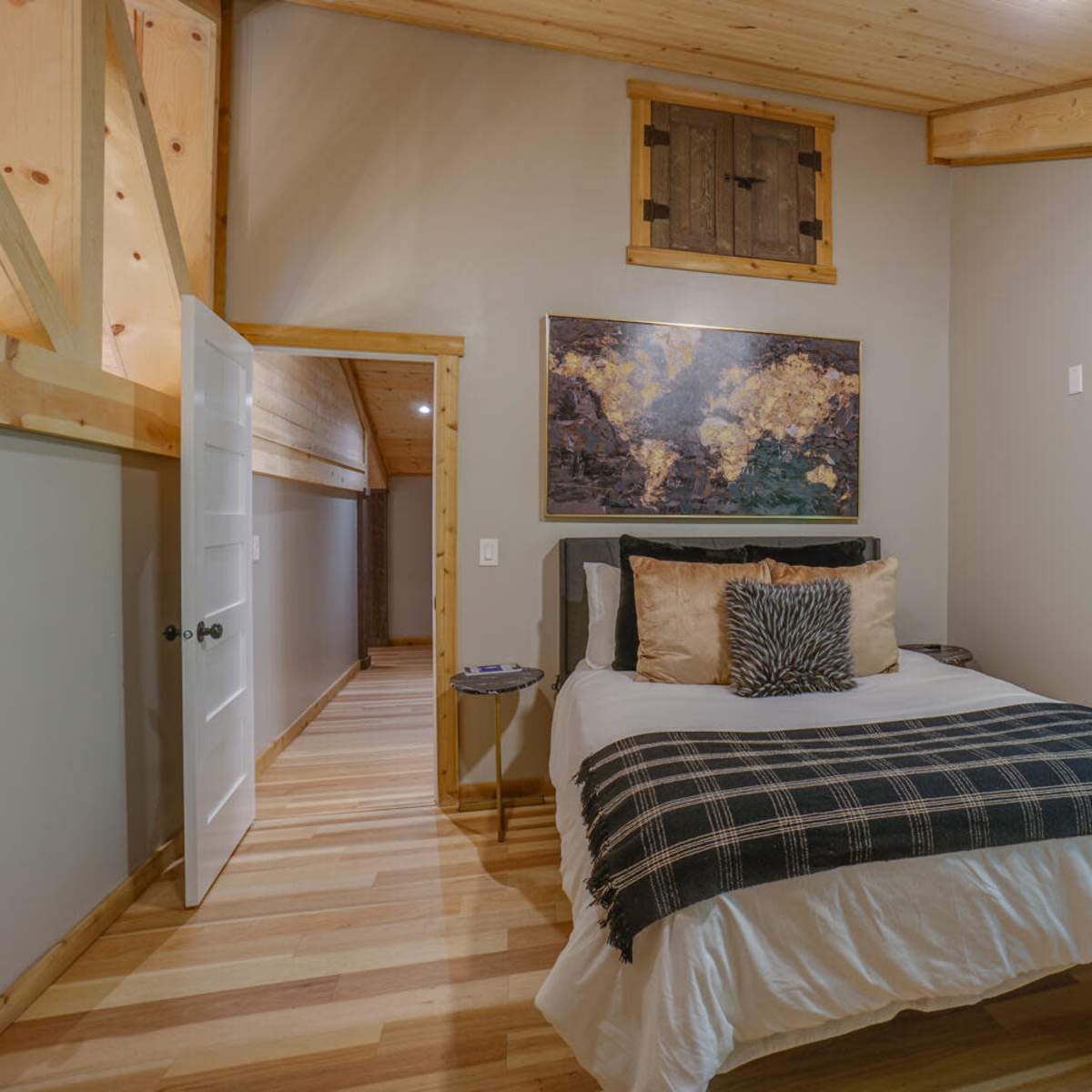 A cozy bedroom with a bed, a large world map on the wall, natural wood finishes, and a window overlooking greenery.
