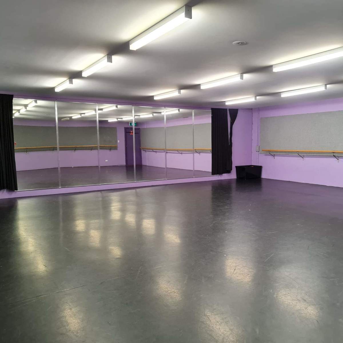 A dance studio with gray flooring, purple walls, and mirrors along one side.