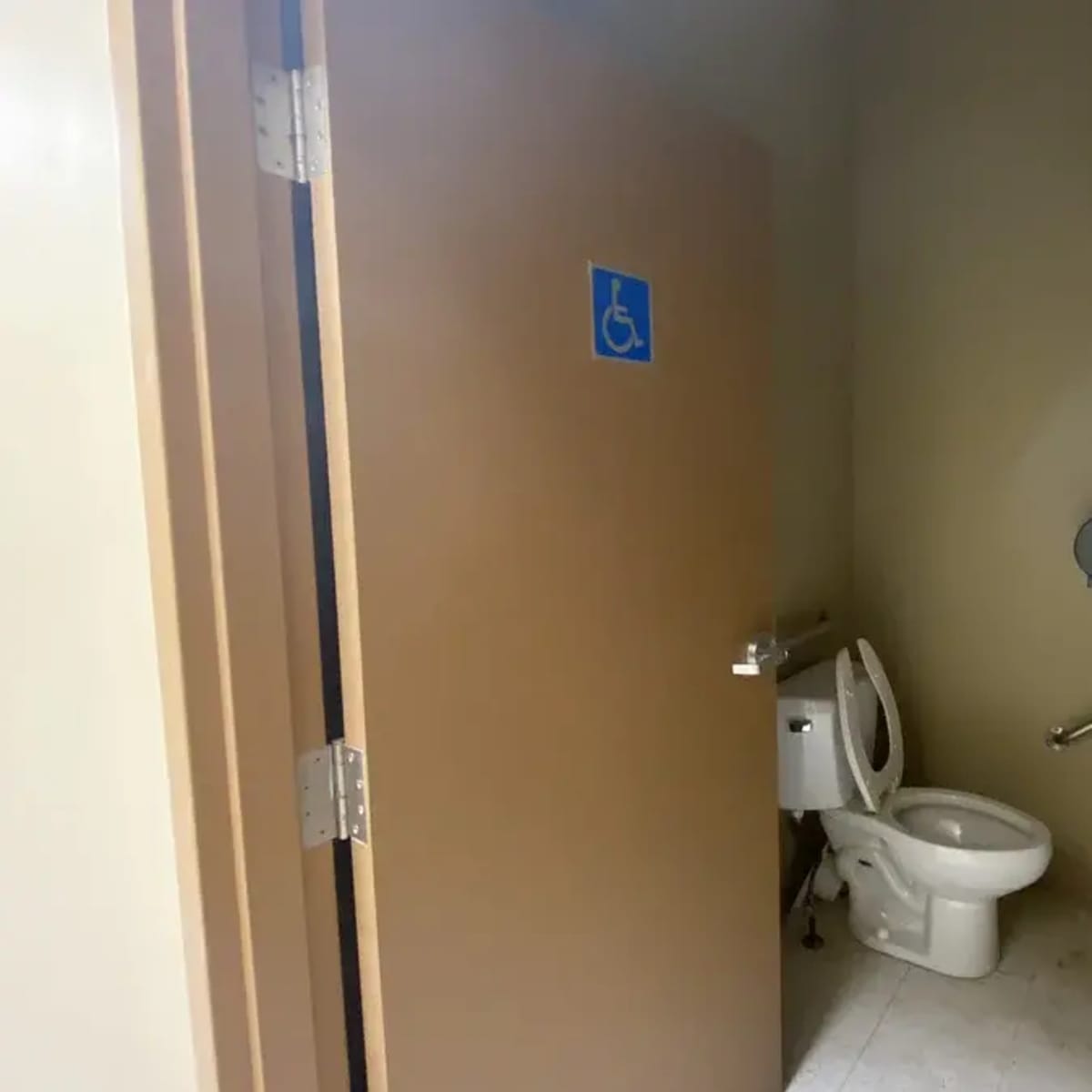 A partially open door to a single restroom, featuring a toilet and an accessible sign.