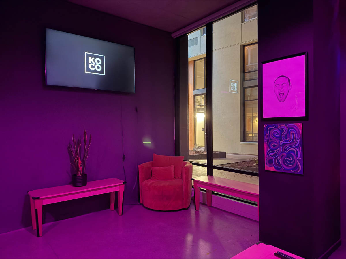 The image shows a modern interior with purple lighting, featuring a curved red chair, a small table, and a wall-mounted TV displaying the logo "KOCO."