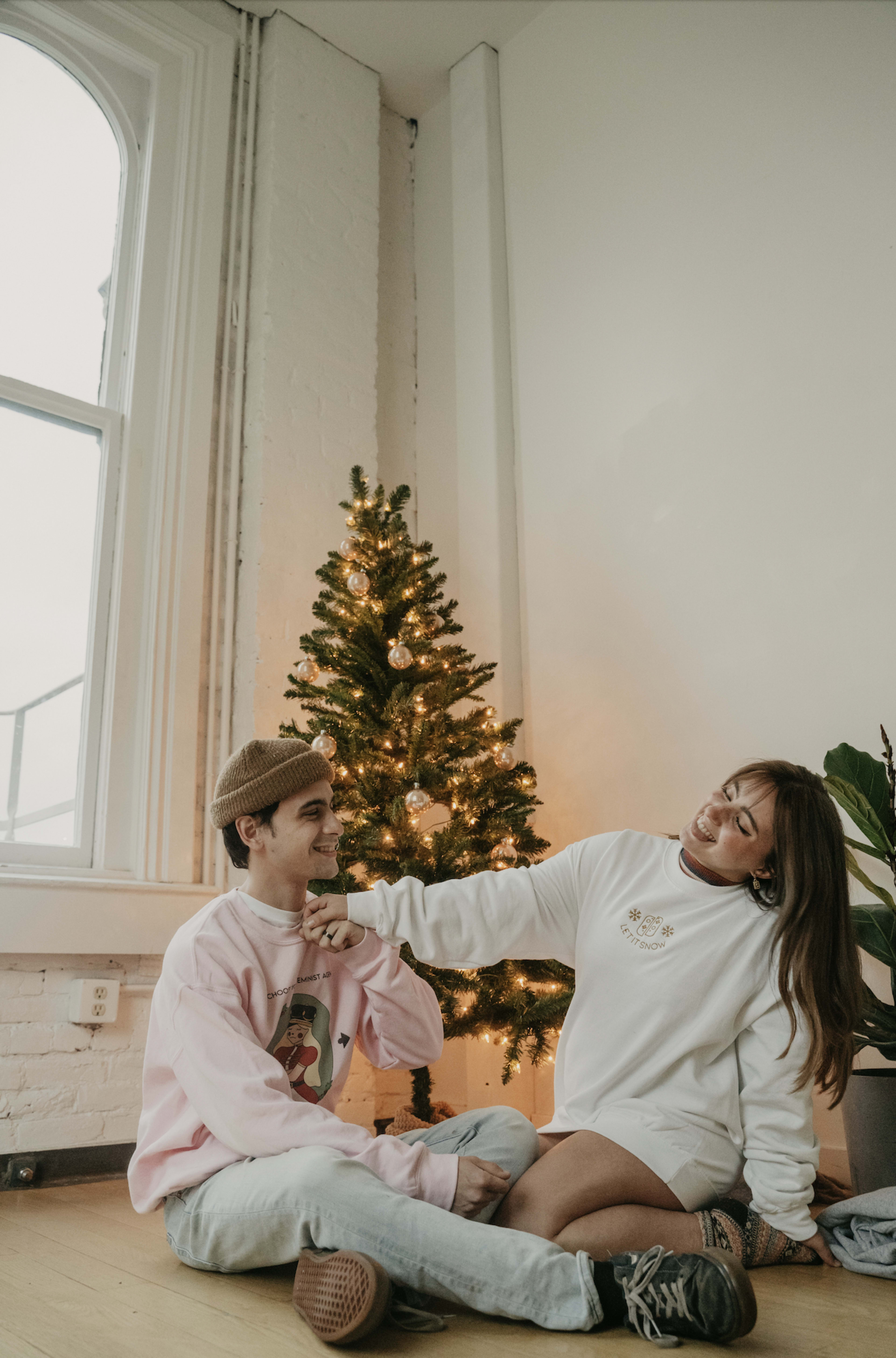 Ein Paar sitzt im Winter neben einem rosa-weißen Weihnachtsbaum für ein Fotoshooting im Stil der 1990er Jahre.