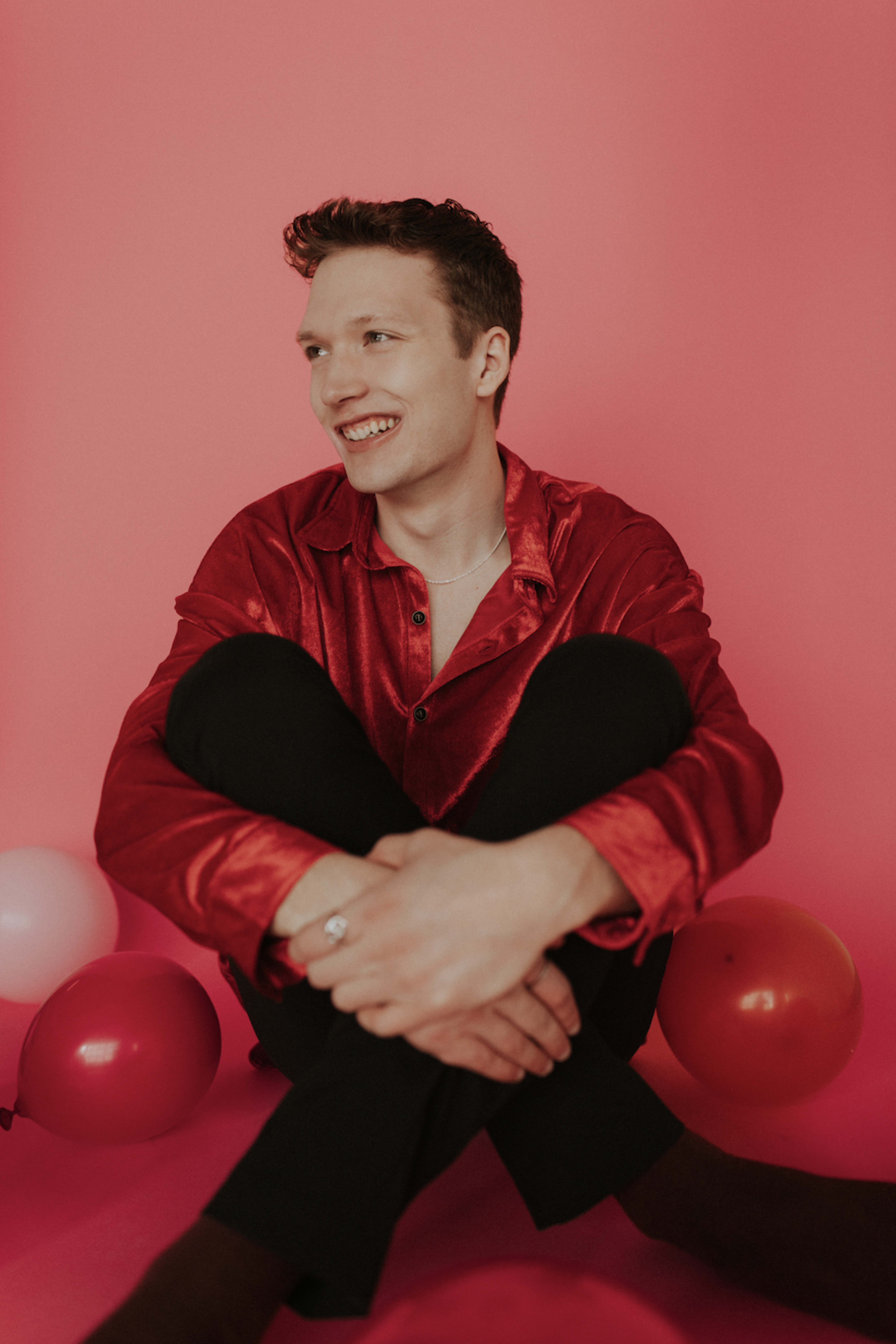 A fashion photoshoot of a person on the floor surrounded by pink and red balloons.