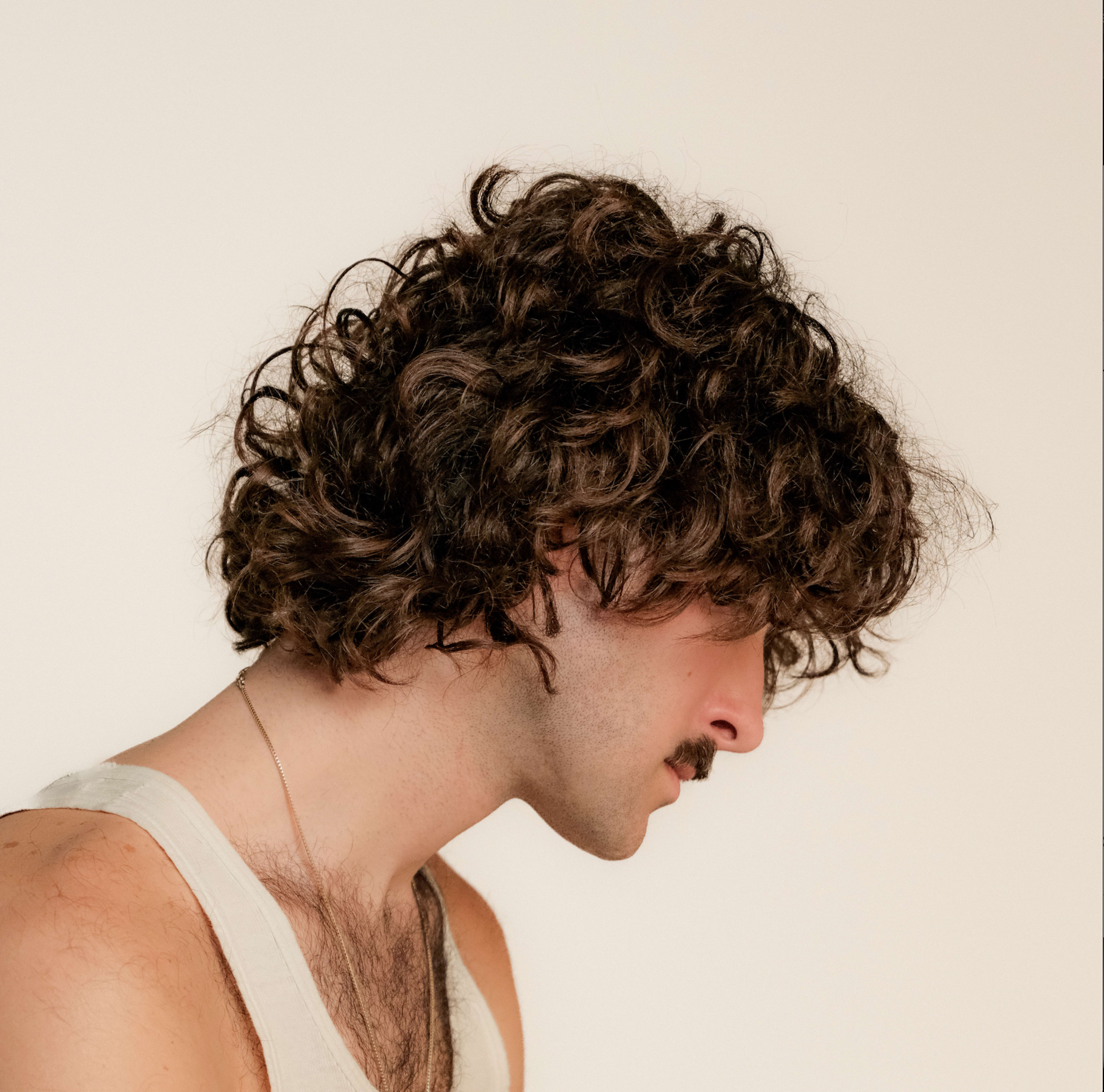 A man with curly brown hair and a moustache for a photoshoot.