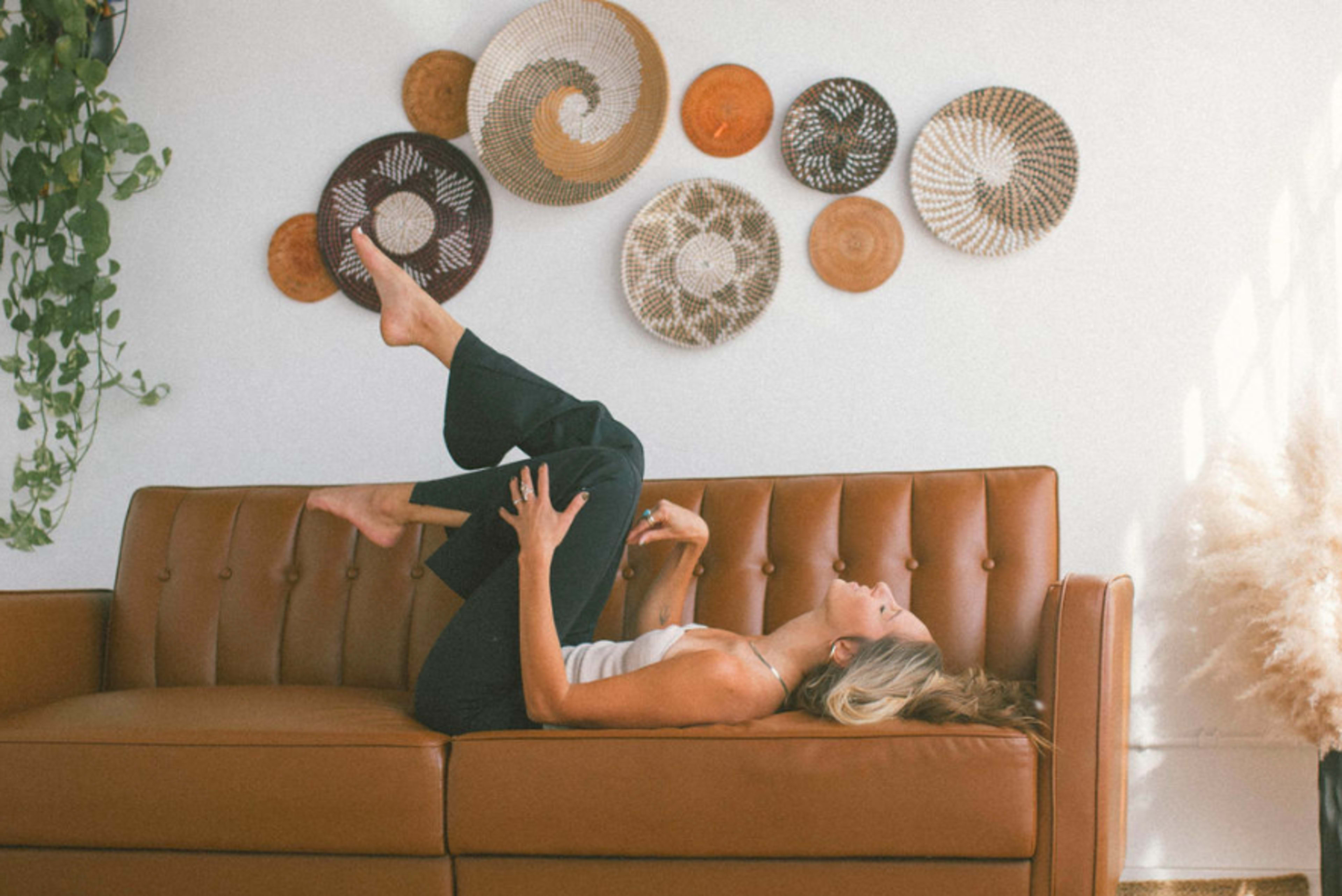 A boho photoshoot of a woman on a brown couch.