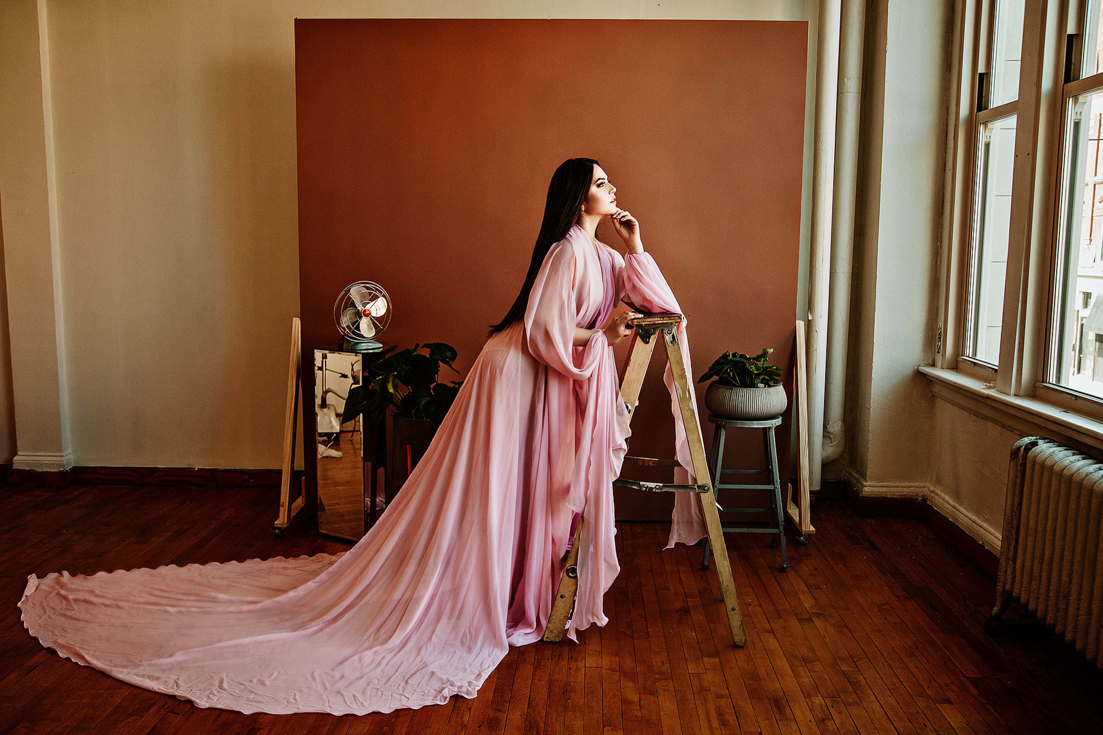 Una mujer con un vestido rosa posando para una sesión de fotos de moda en una escalera rodeada de plantas.