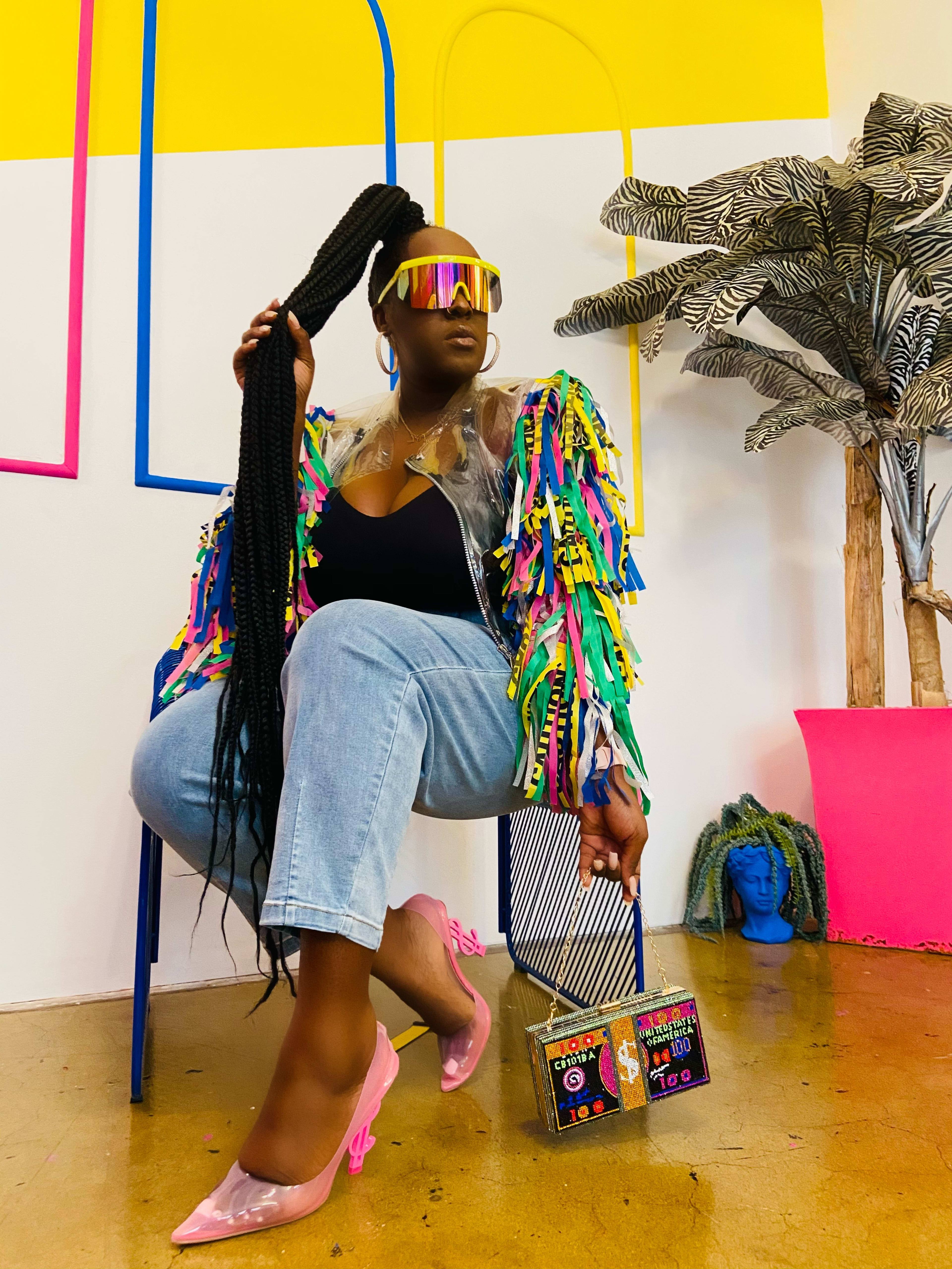 A fashion photoshoot featuring a woman seated in a chair wearing neon sunglasses.