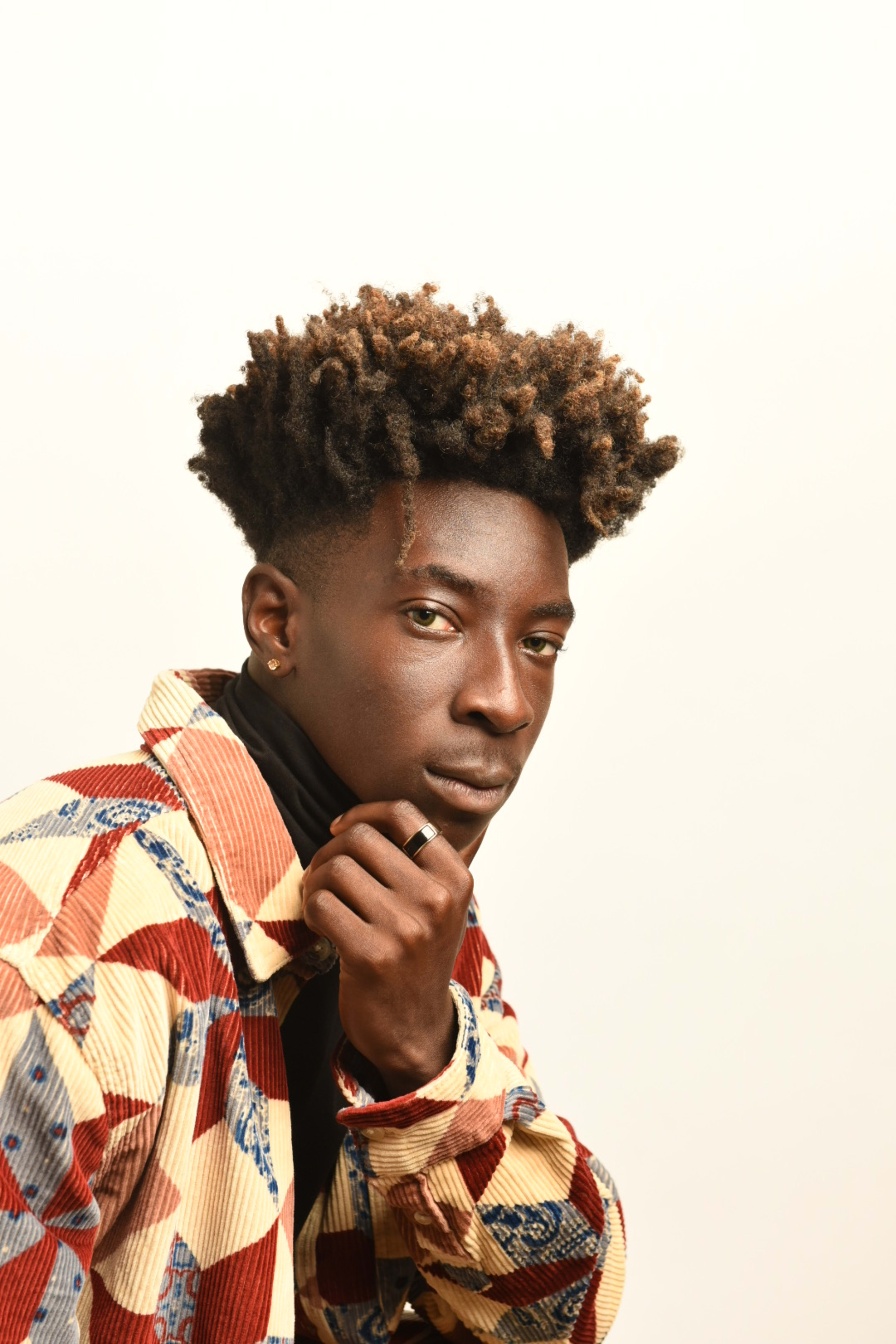 A man with curly hair wearing a colorful shirt for a photoshoot.