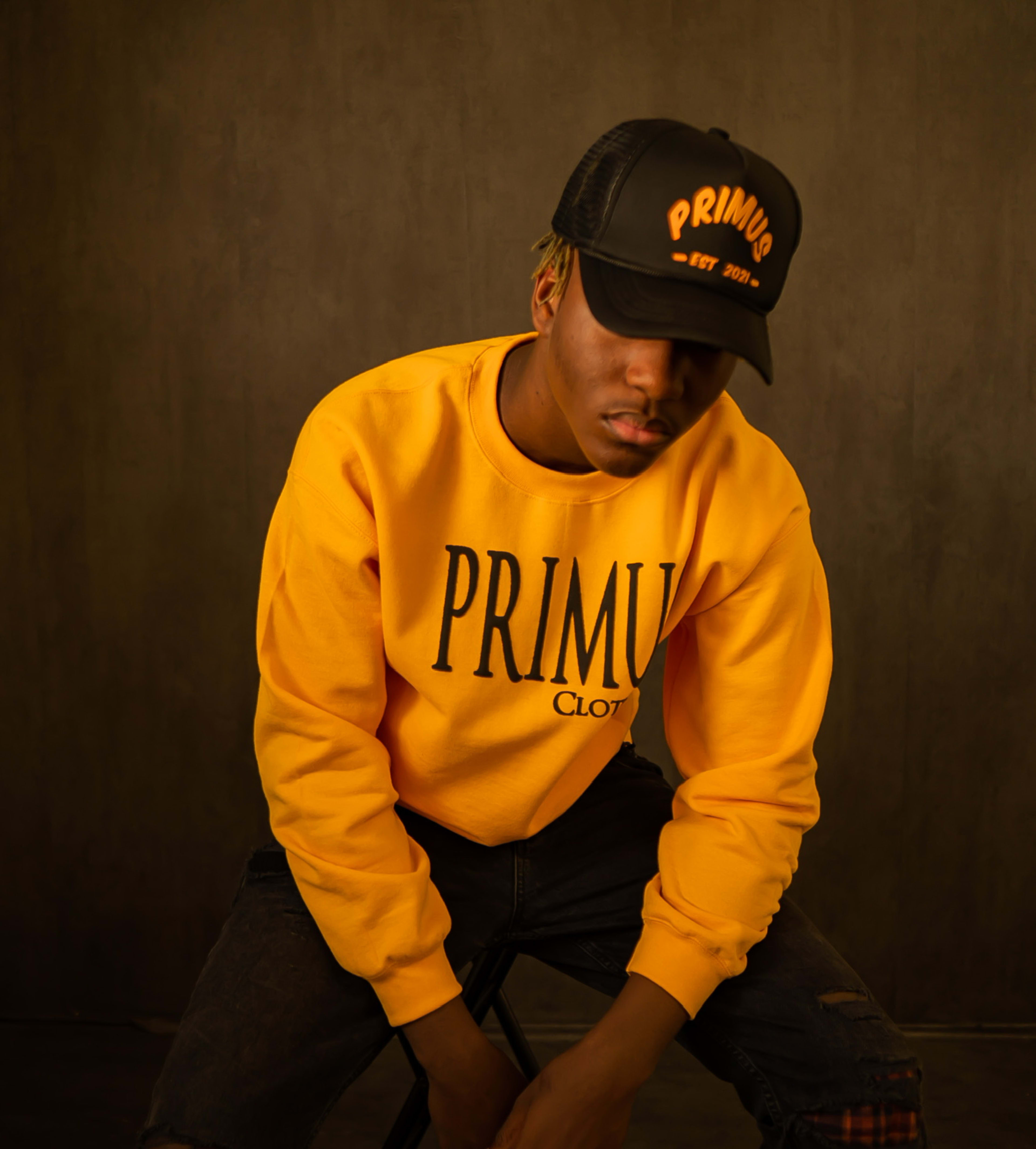 A man in a yellow sweatshirt posing for a photoshoot wearing a black hat.