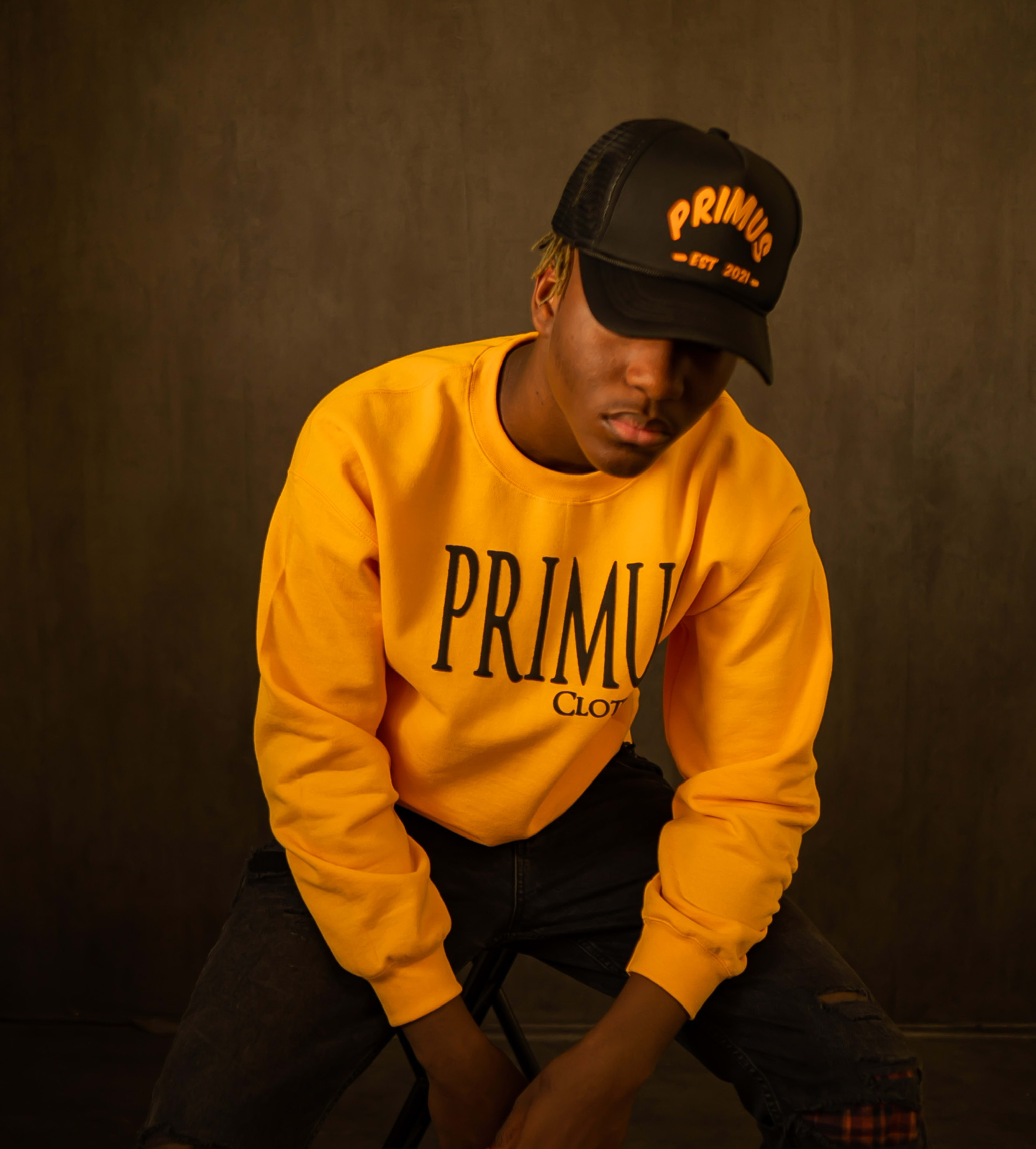 A man in a yellow sweatshirt posing for a photo shoot wearing a black hat.