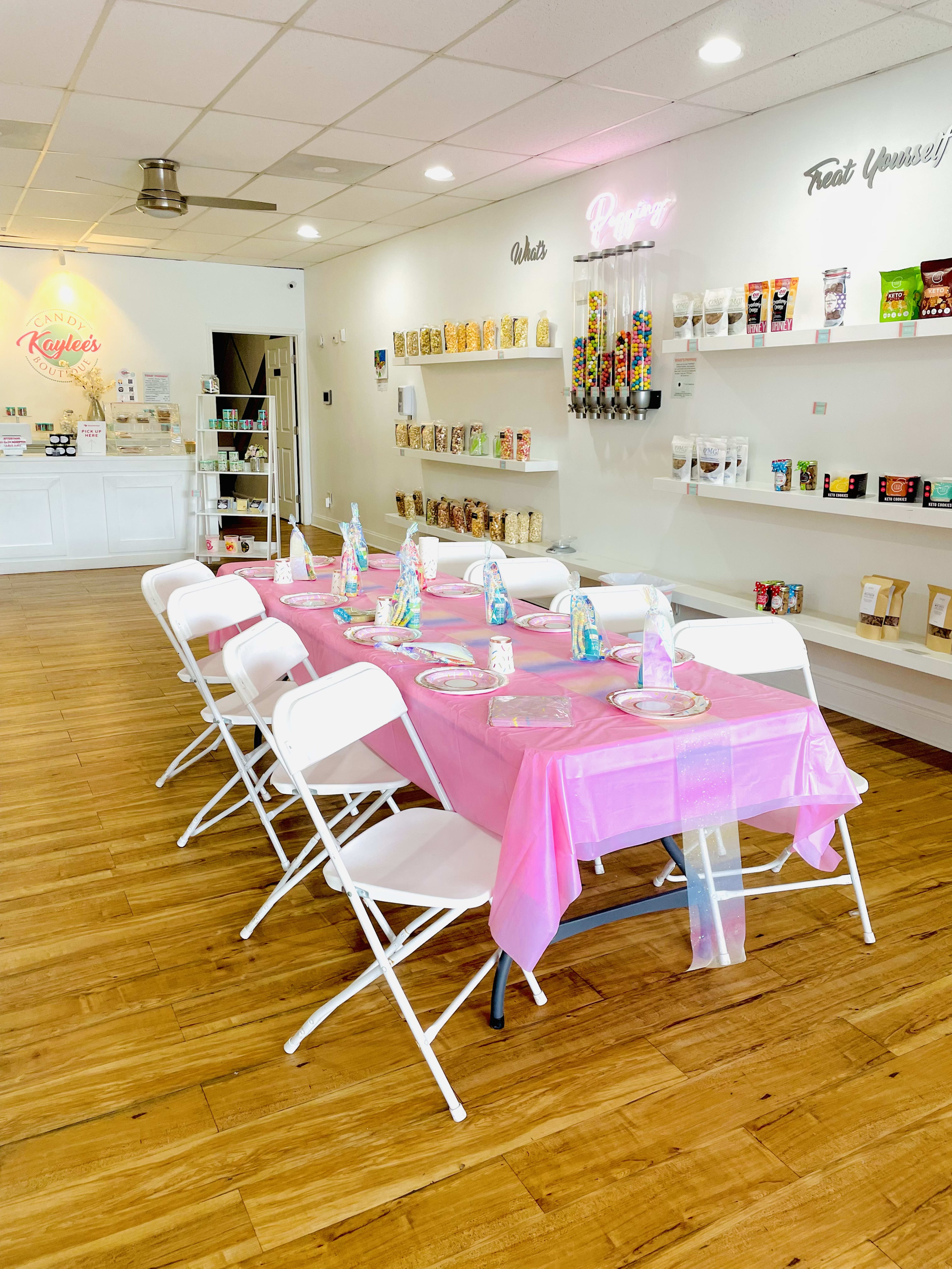 A candy-themed birthday party room with a pink table and white chairs.