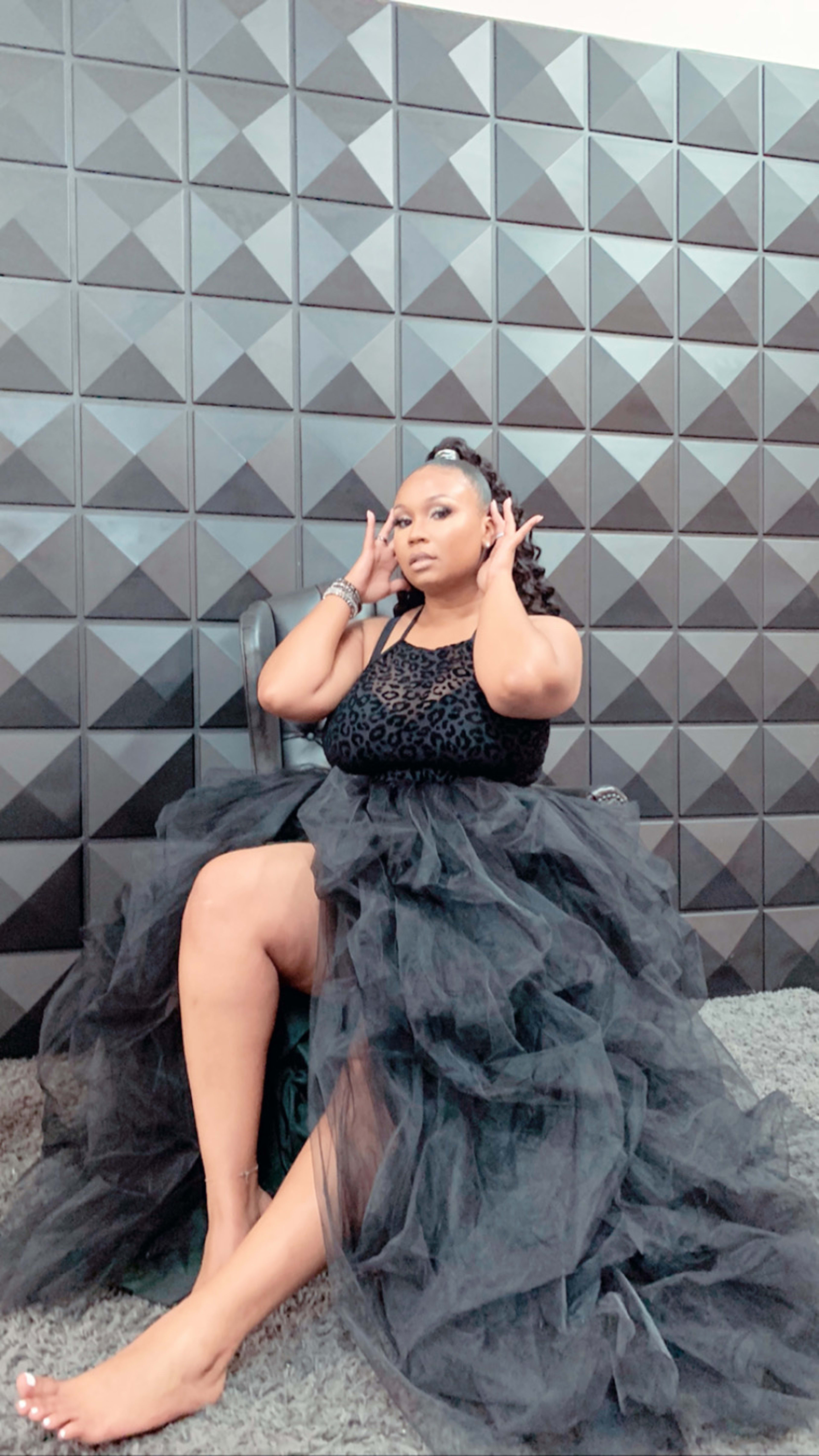 A woman in an all black dress sitting on a chair for a photoshoot.