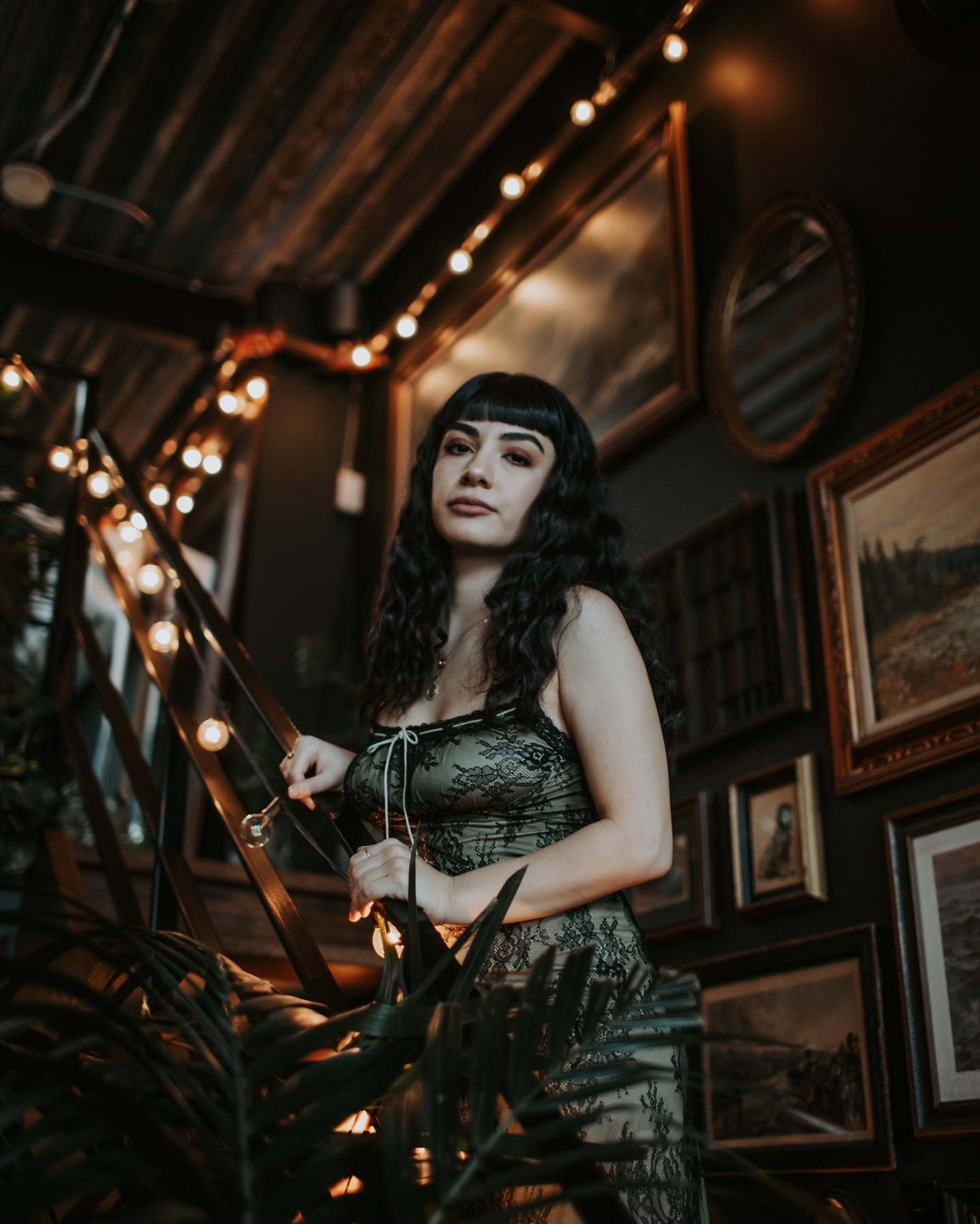 A fashion photoshoot with a woman in a green dress posing next to a staircase surrounded by plants.