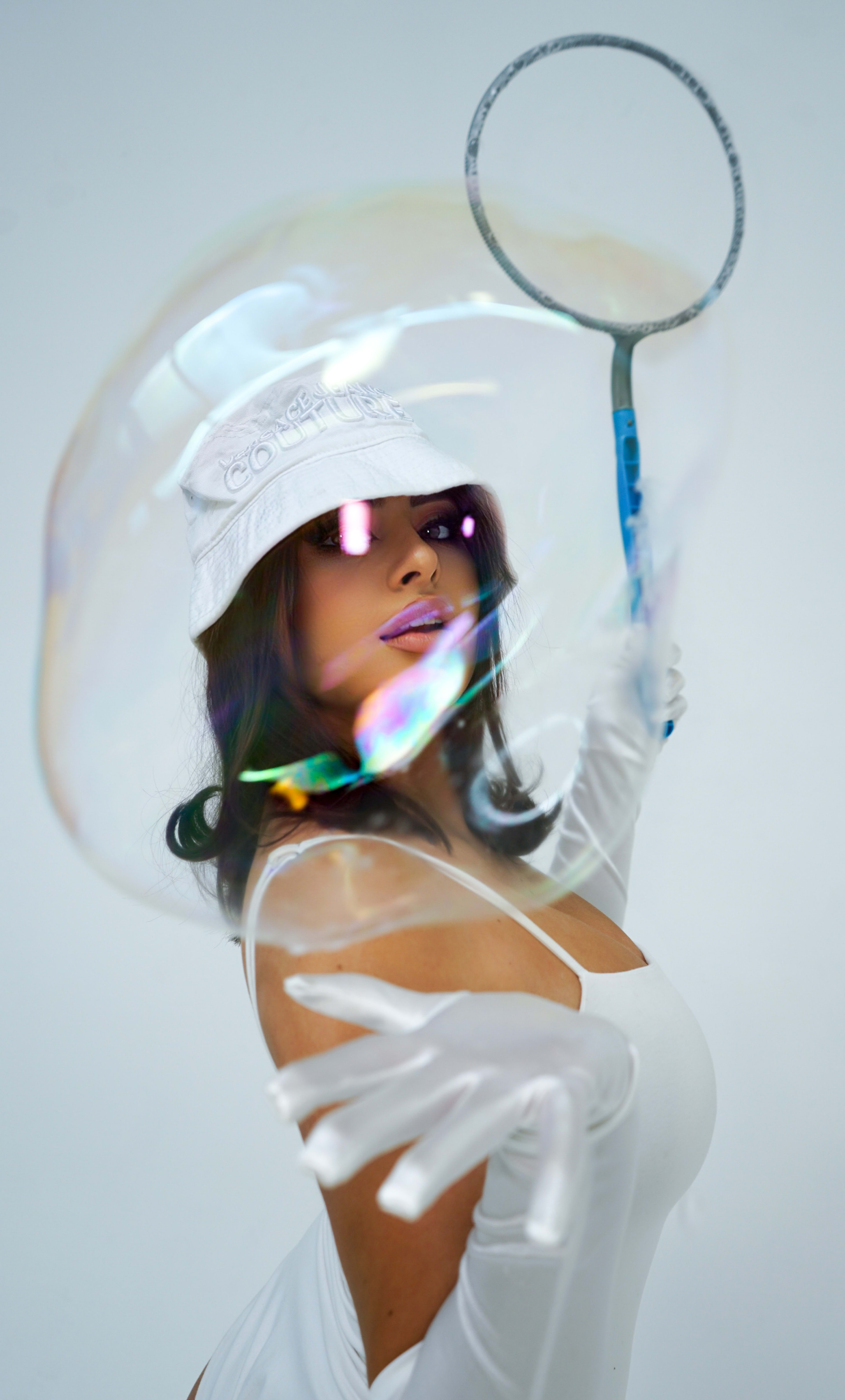 A fashion photoshoot featuring a woman in a white dress and holding big bubble wand.
