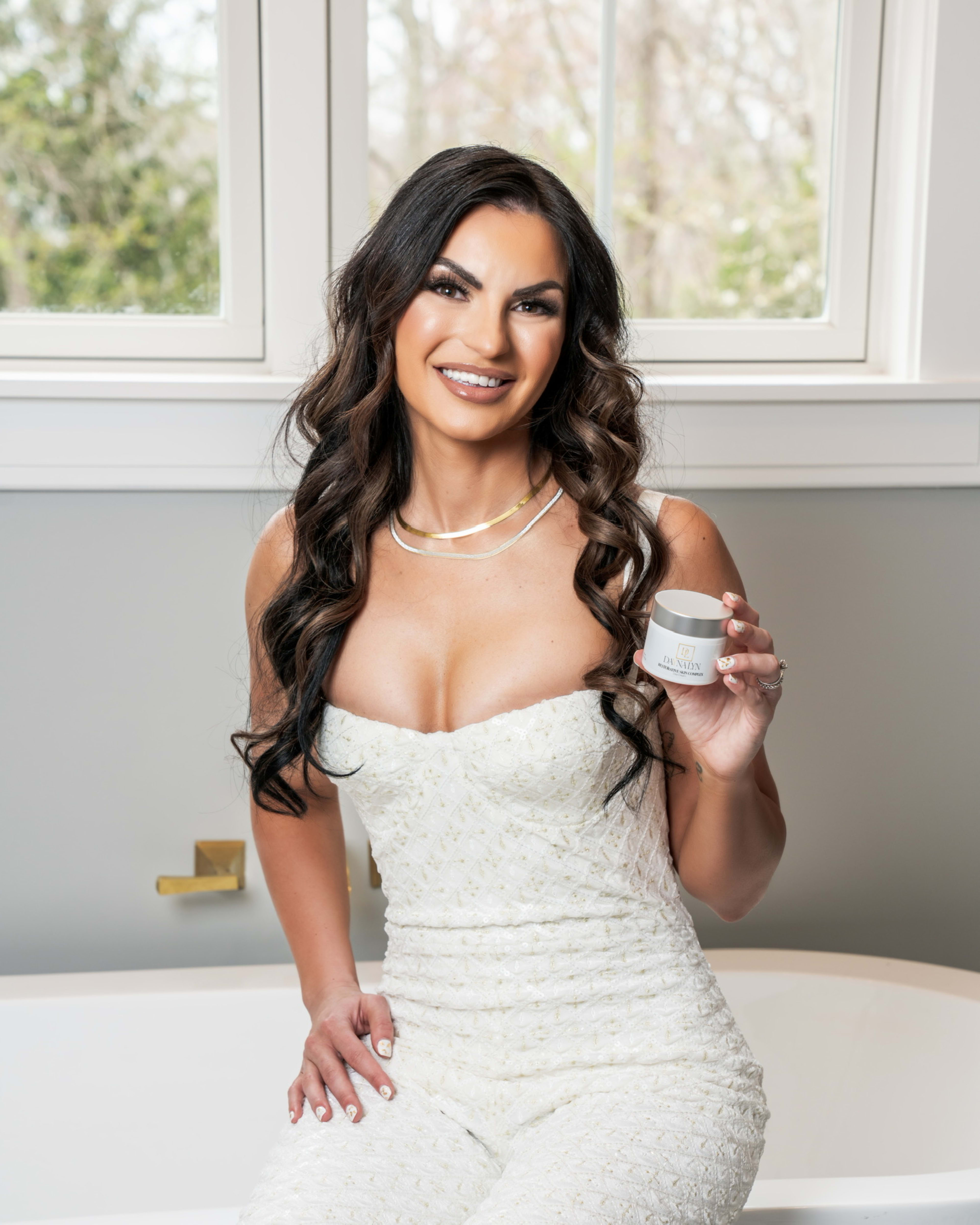 A photoshoot of a woman in white holding a jar of cream.