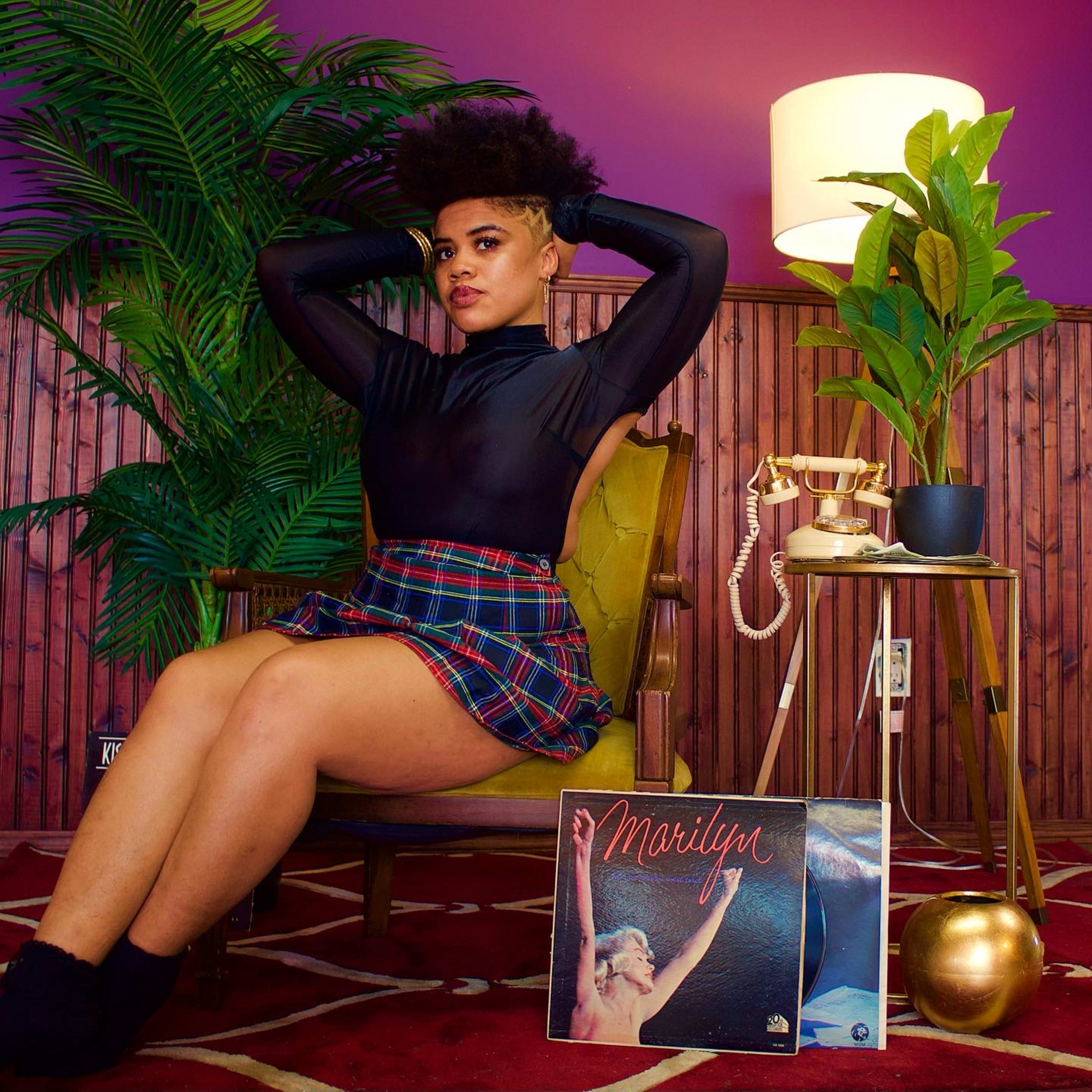 A retro photo shoot of a woman sitting on a chair in a room surrounded by plants.