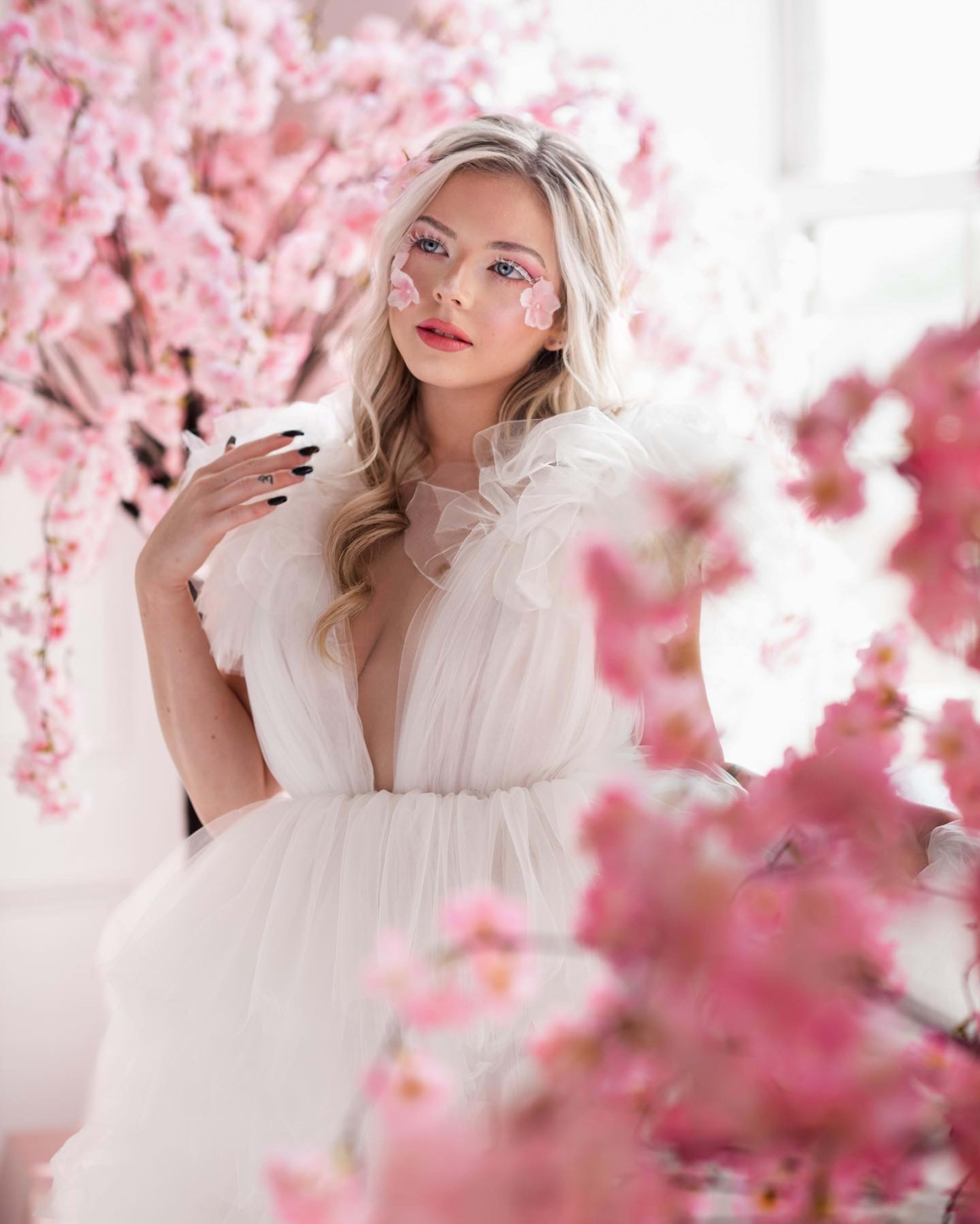 A spring fashion photo shoot featuring a woman in a white dress posing in front of pink flowers.