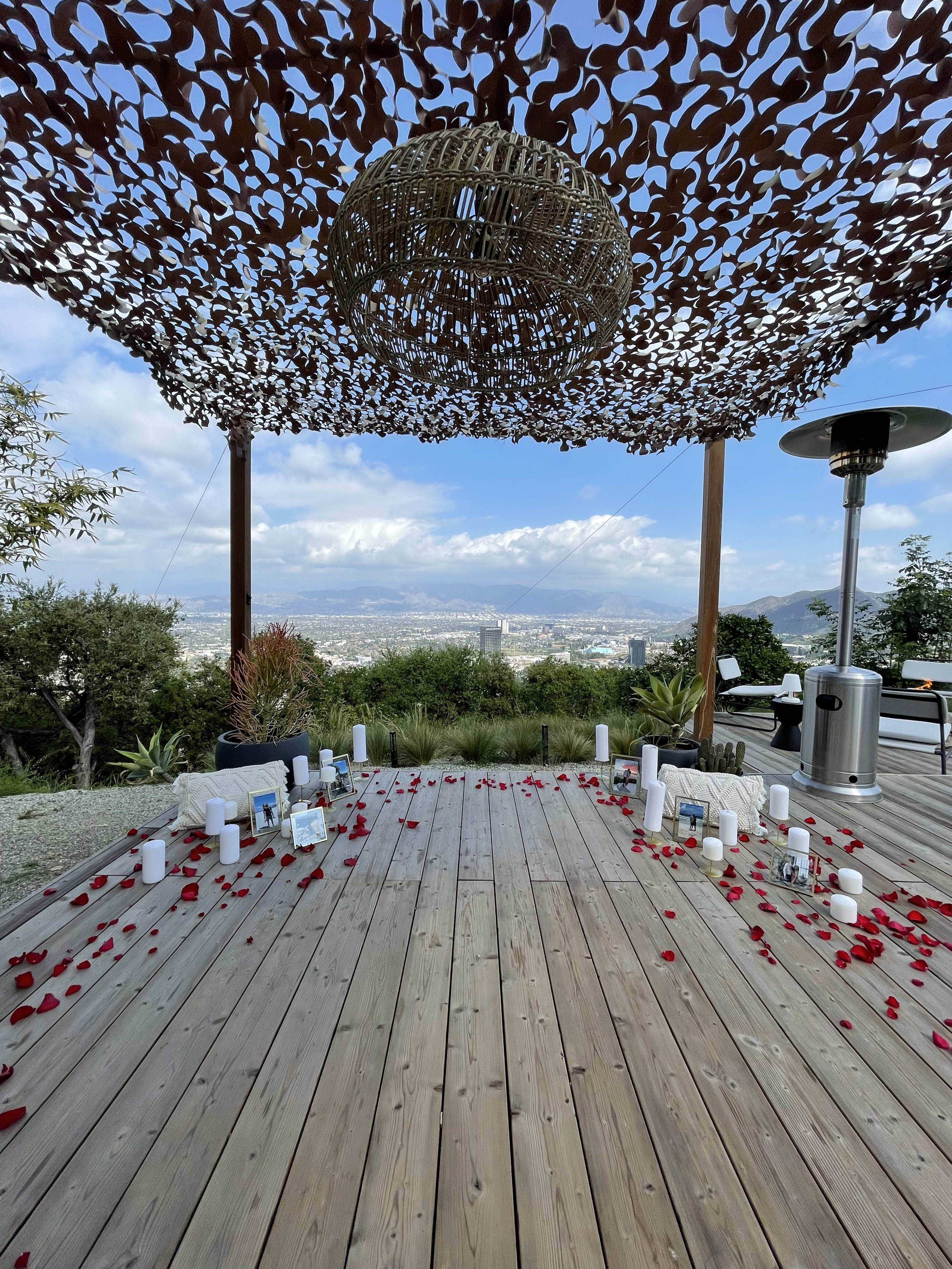 Una terraza al aire libre con pétalos de rosa y velas preparada para un compromiso.