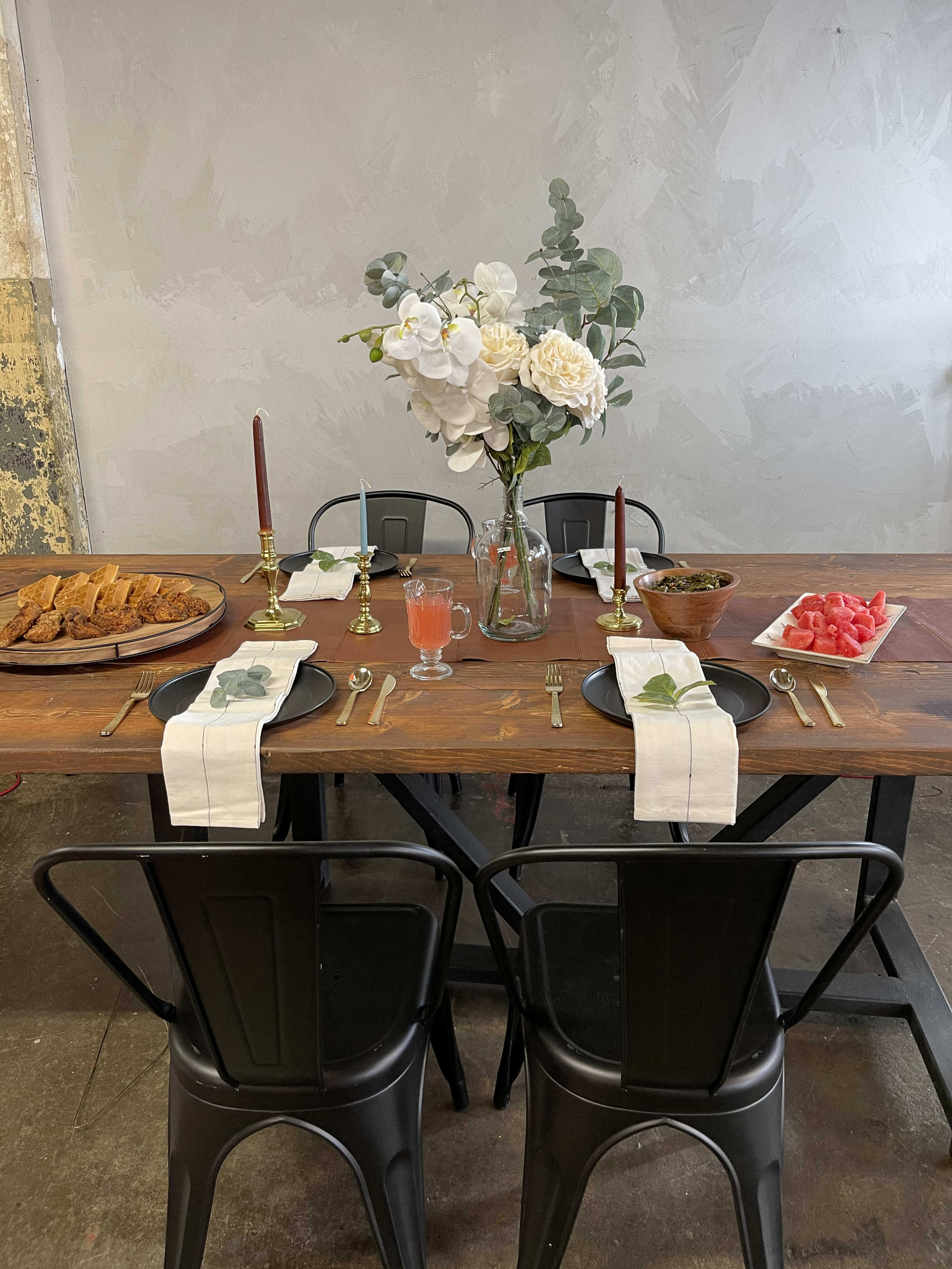 A rustic wooden table with black chairs and a vase of flowers.