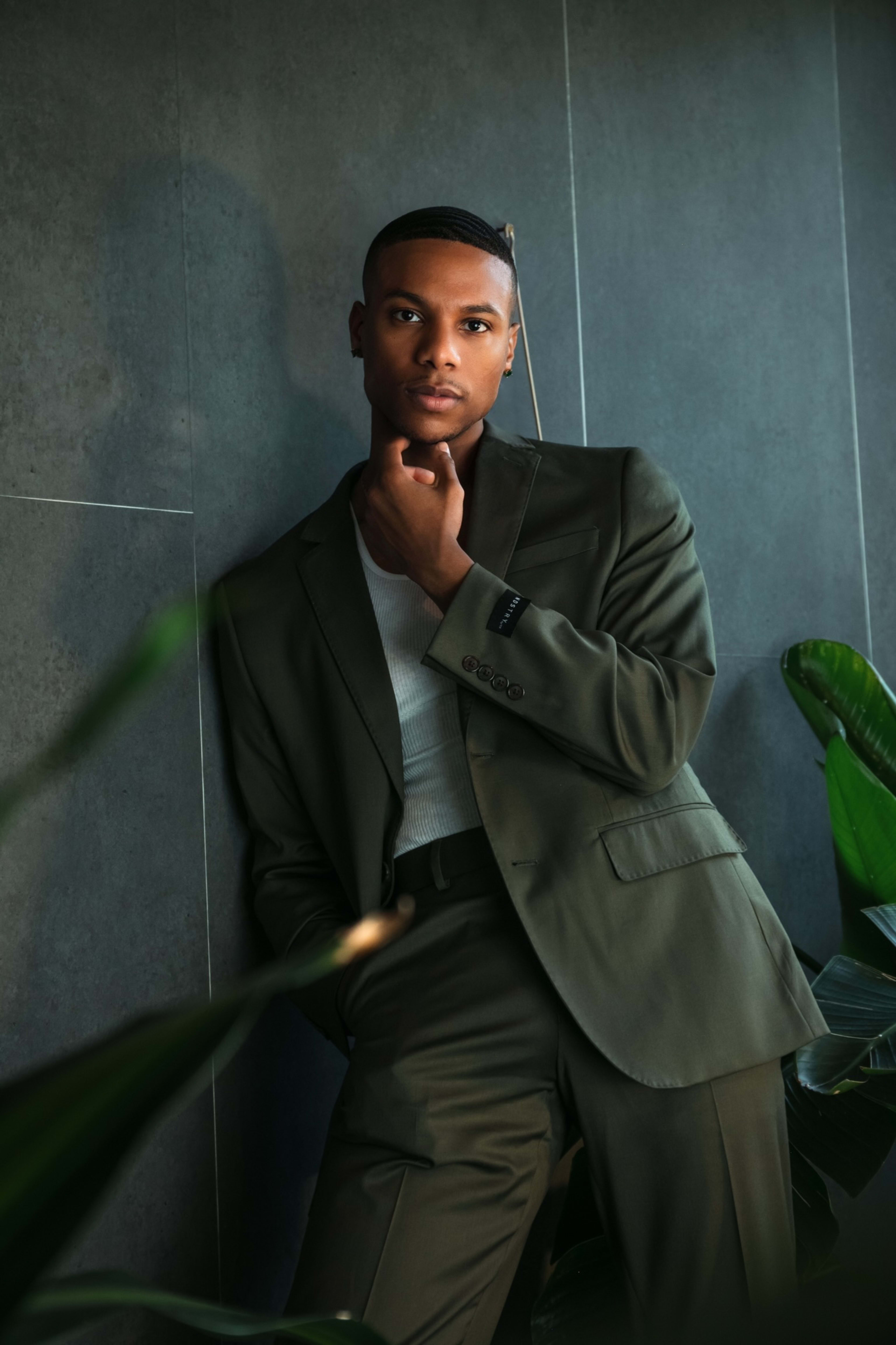 A man in a green suit leaning against a green wall for a fashion photoshoot.