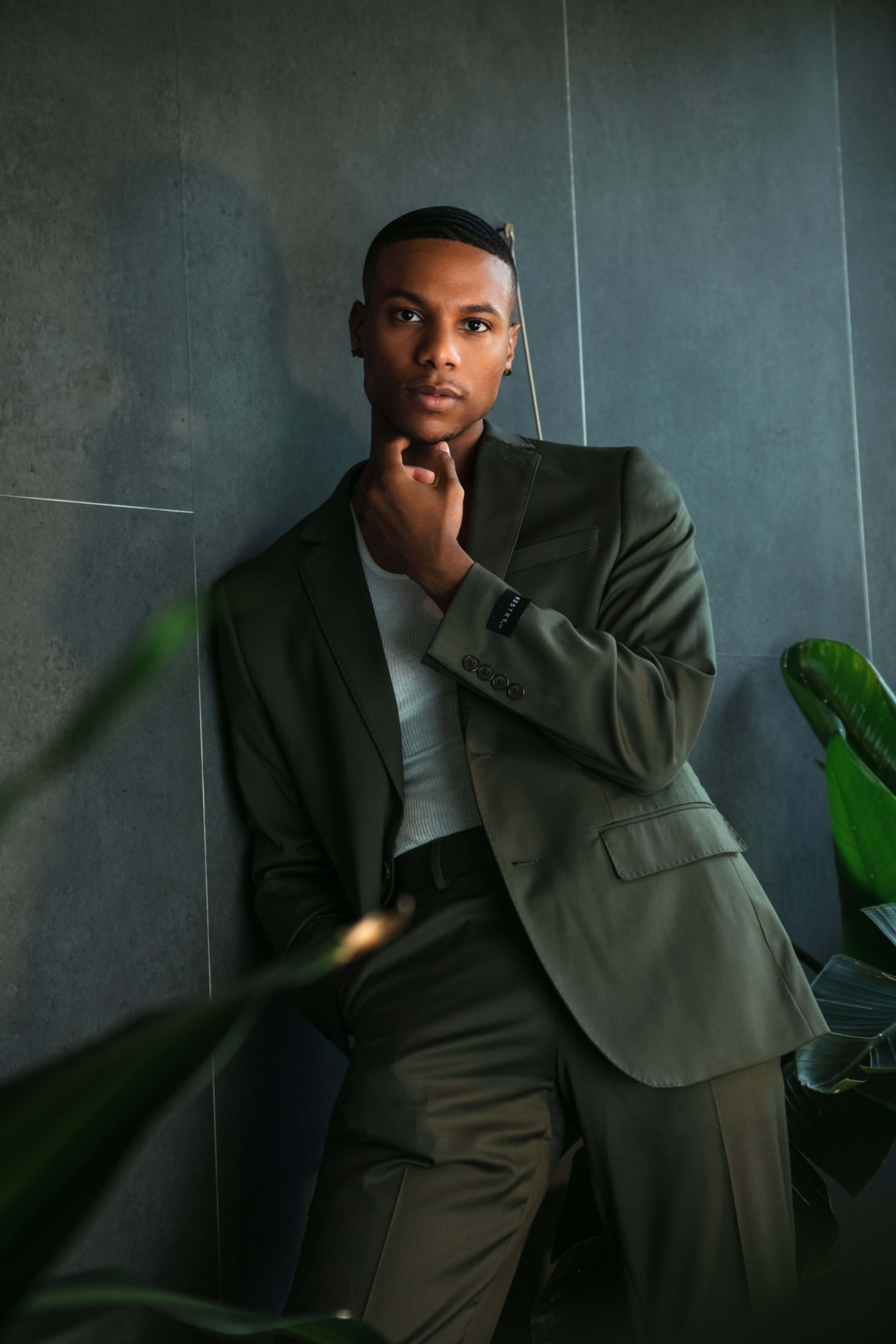 A man in a green suit leaning against a green wall for a fashion photo shoot.