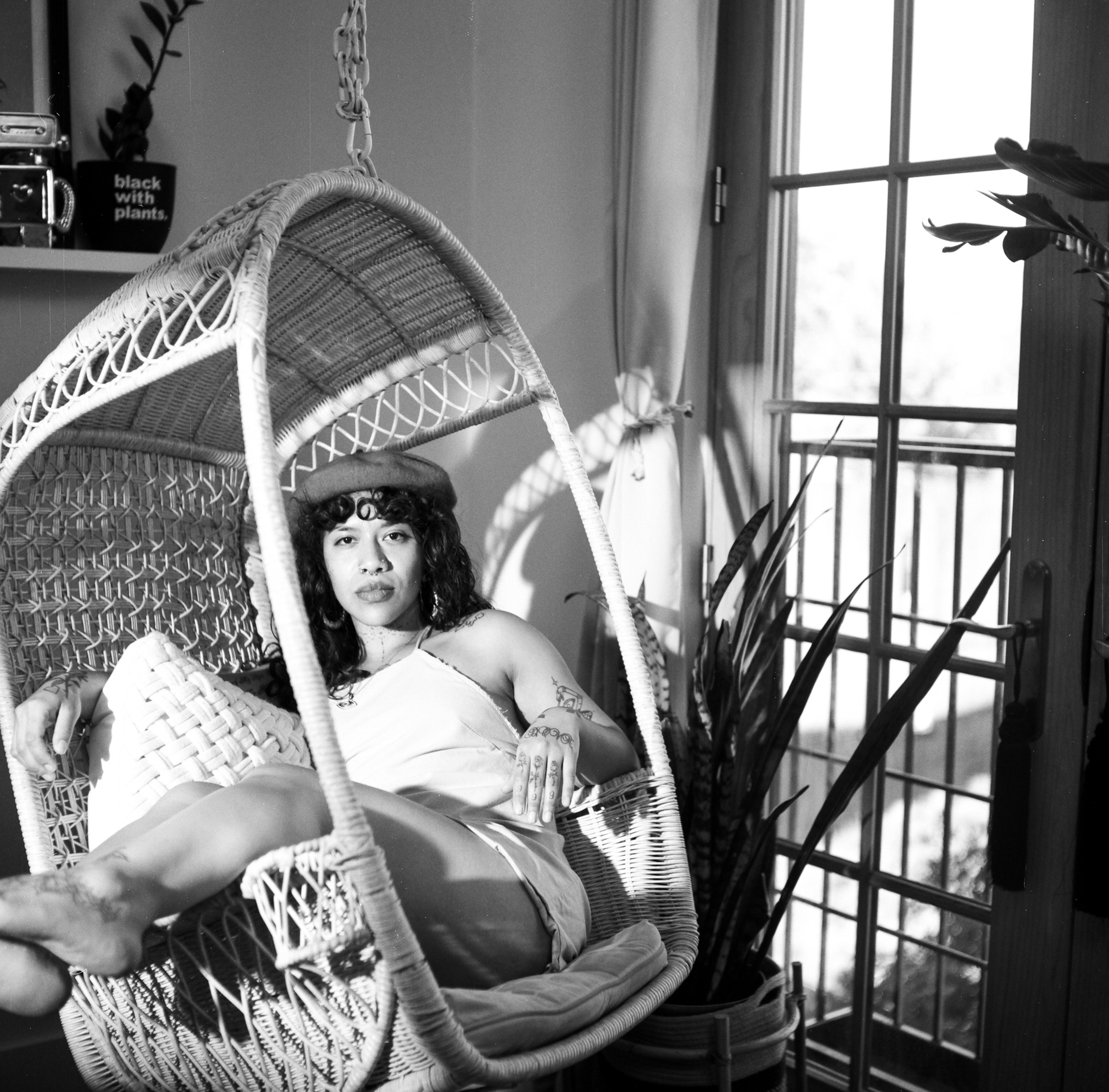 A woman lounging in a boho wicker swing chair surrounded by plants.