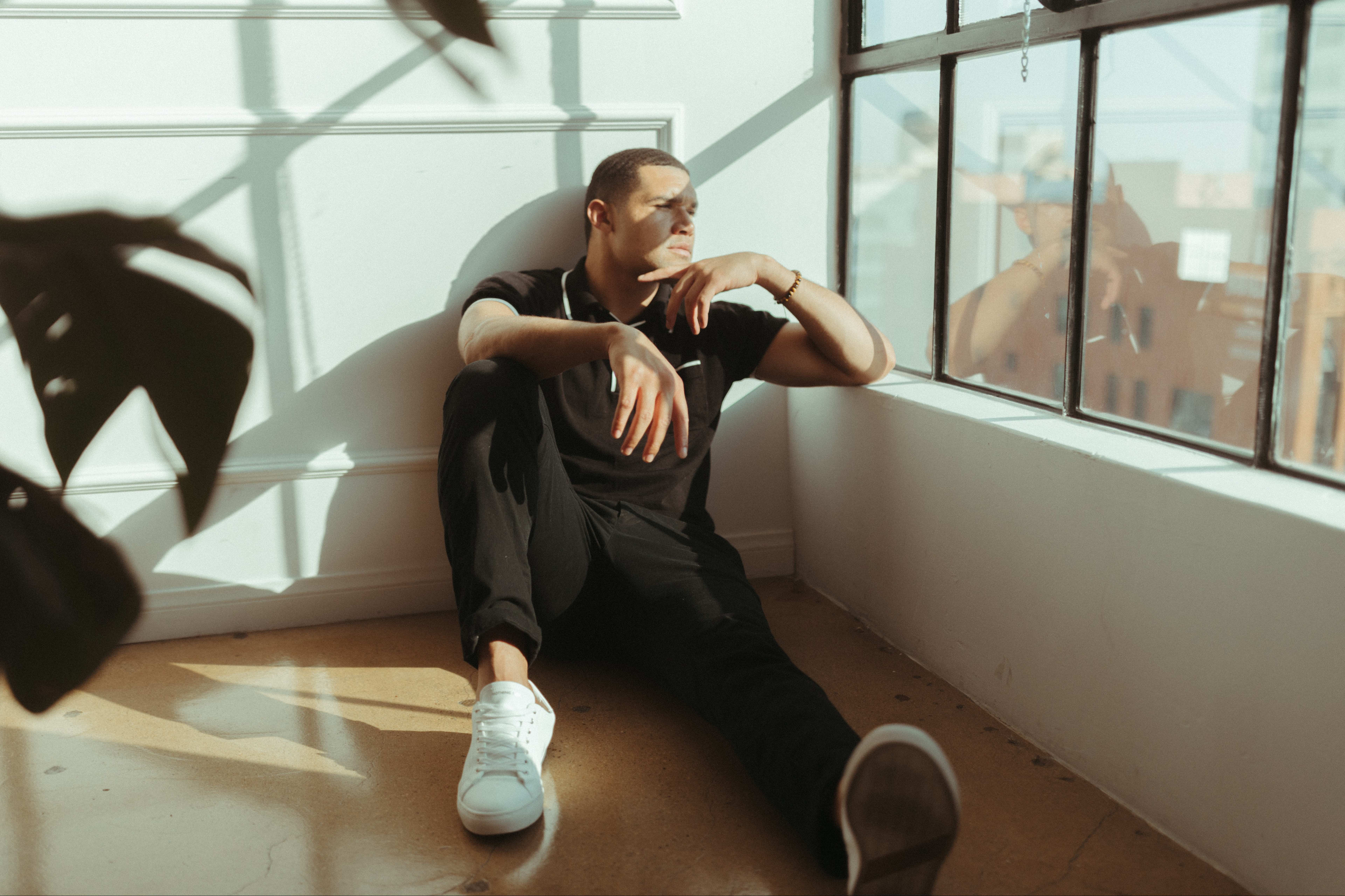 a minimal man sitting on the floor in front of a window.