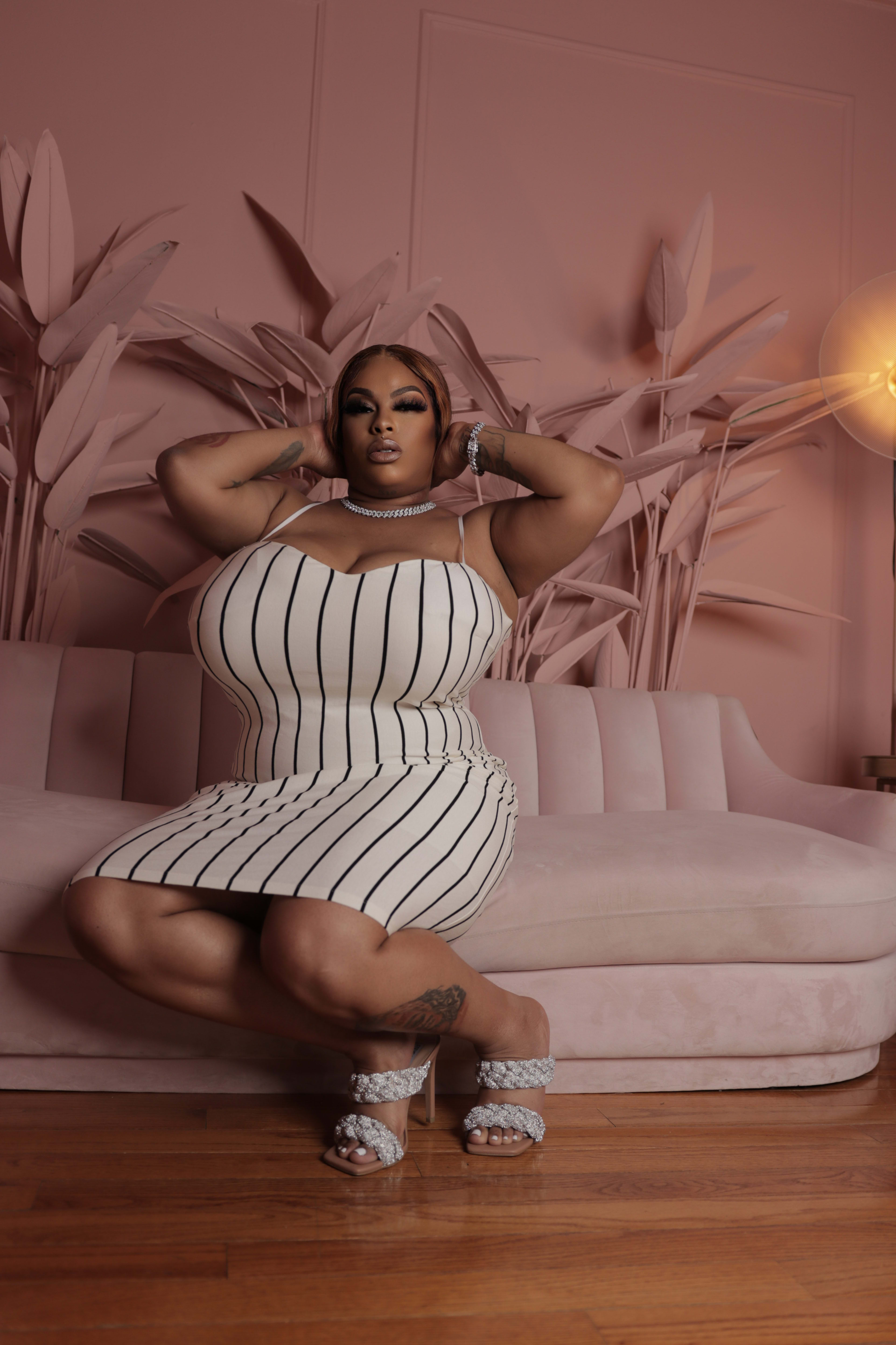 A woman in a striped dress posing for a fashion photo shoot on a pink couch.
