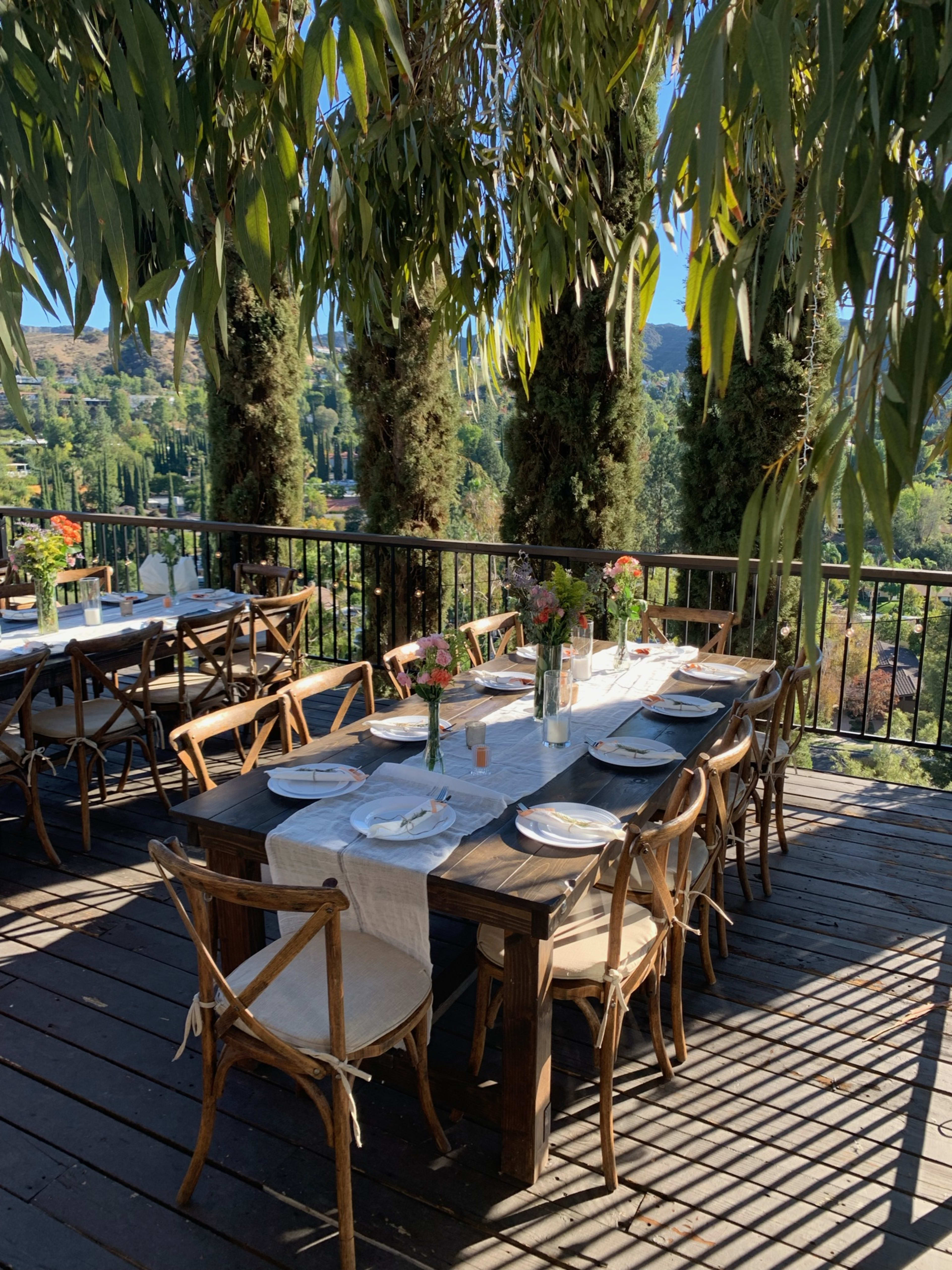 A table on a deck set up for an outdoor engagement party surrounded by plants.