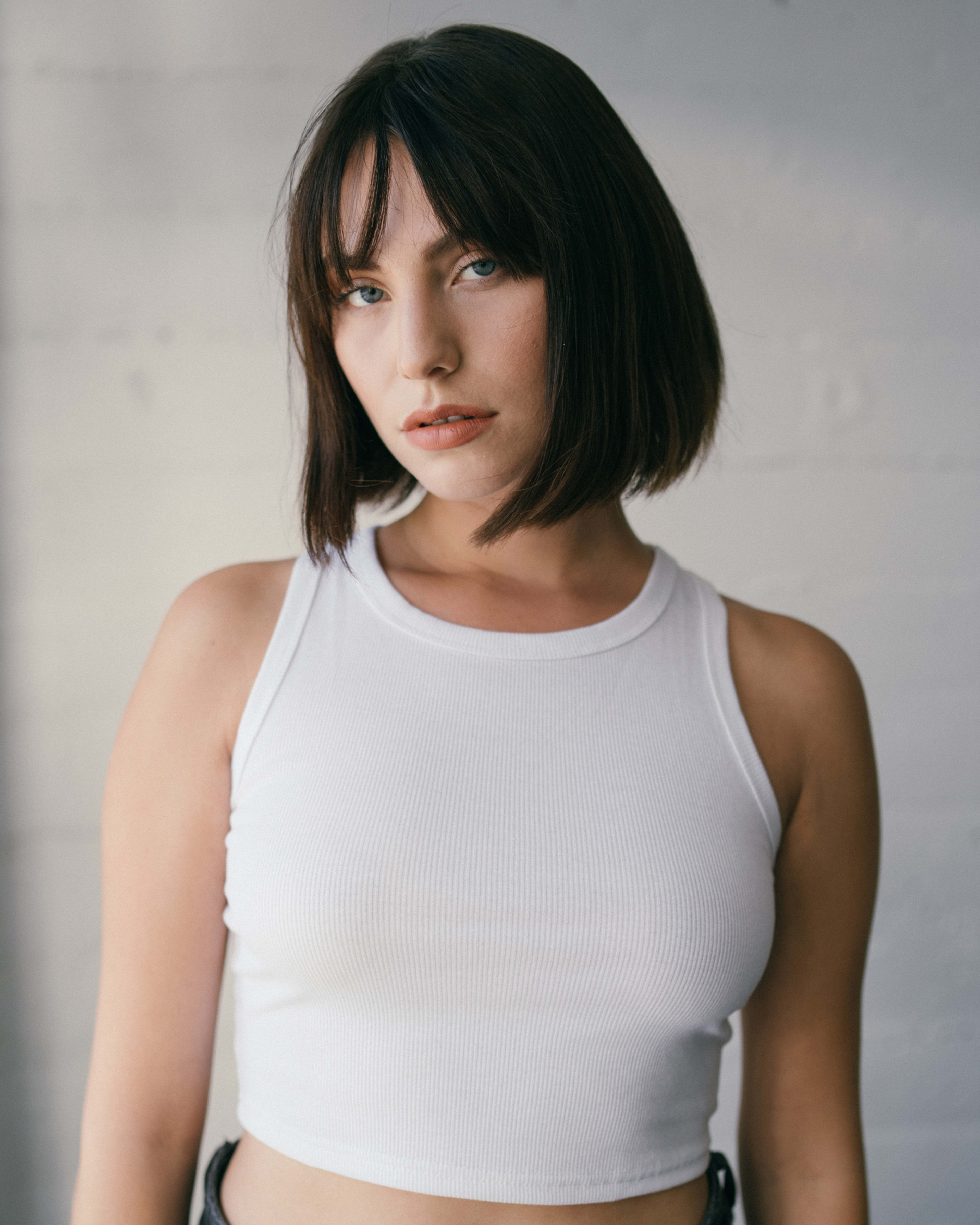 Eine Frau in einem weißen Crop-Top posiert für ein minimalistisches Porträtfoto.